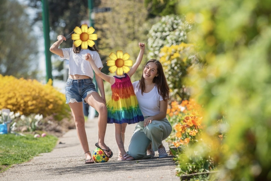 Cayley crouching on a garden path in spring, cheering with two children among the flower beds.