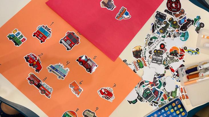 Numbered fire-truck and rescue-vehicle stickers arranged on coloured paper for a counting activity.
