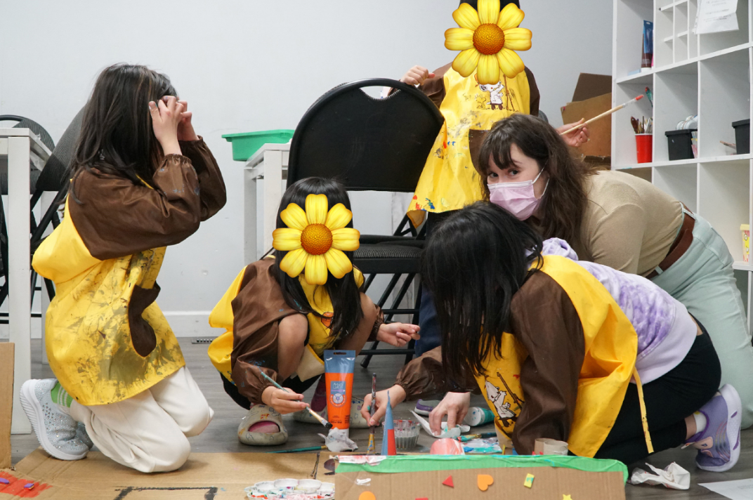 Children in painting smocks kneeling on the floor to paint rocks together with Cayley.