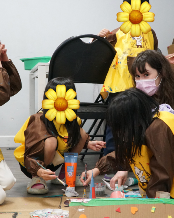 Children in painting smocks kneeling on the floor to paint rocks together with Cayley.