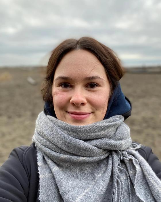 Cayley Burton outdoors on an overcast day, wrapped in a grey wool scarf and smiling at the camera.