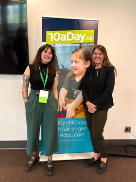 Cayley standing with a fellow advocate in front of a $10aDay.ca banner reading "quality child care with fair wages for educators".