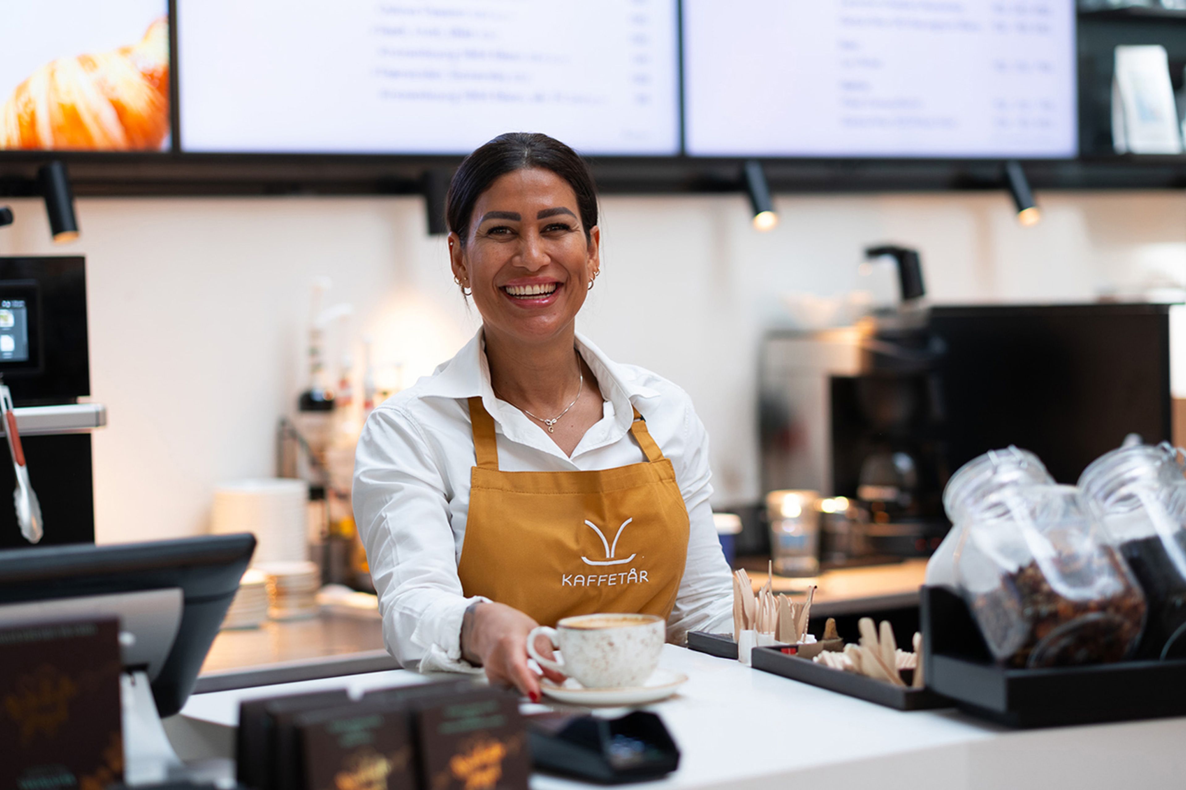 Dame med forkle med logo rekker frem en kopp kaffe