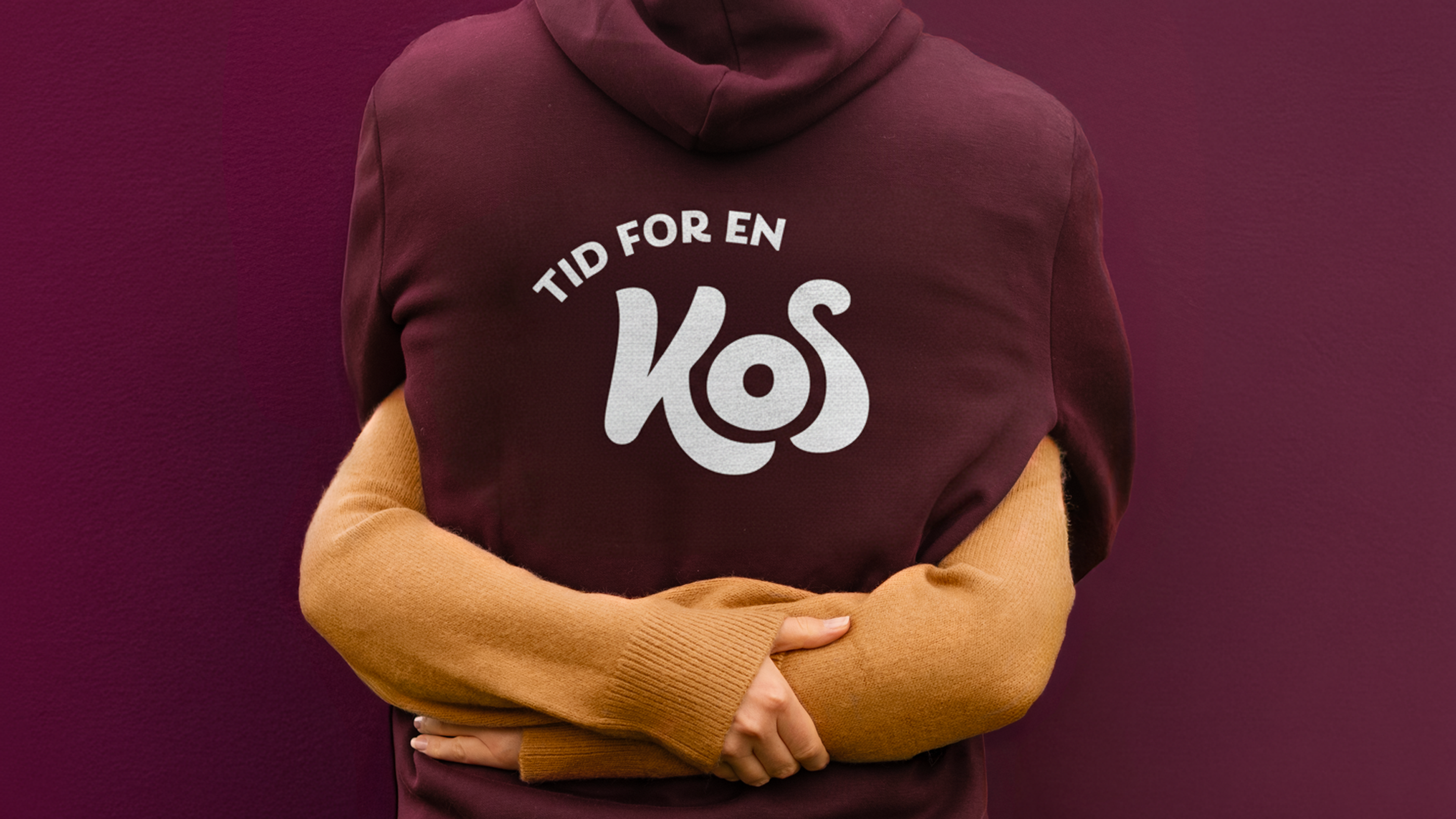 Bildet viser to som klemmer hverandre. Hen ene har genser med kos logo
