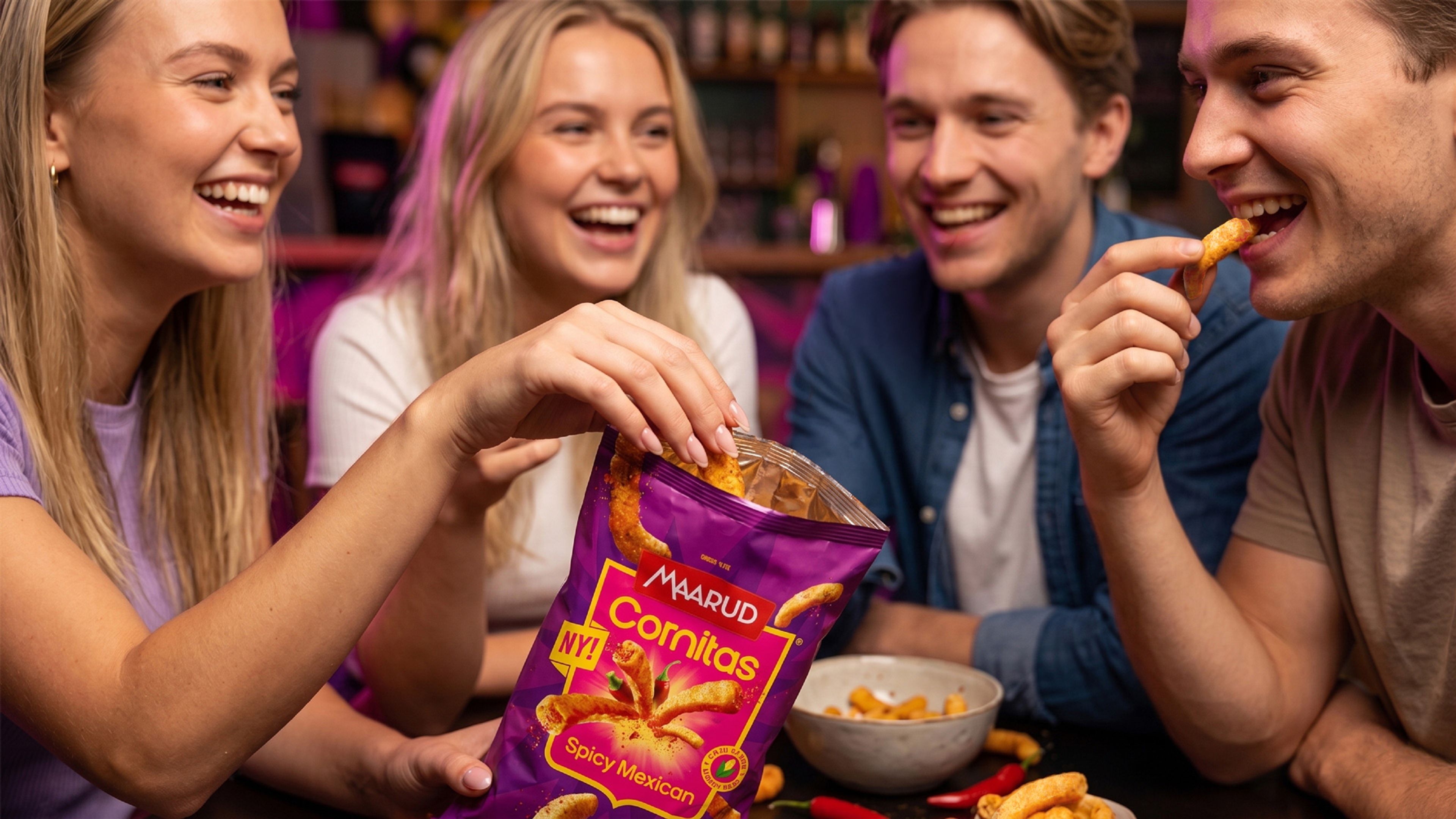 To jenter og to gutter som koser seg med en pose med Cornitas, de sitter rundt et bord og spiser og ler. 