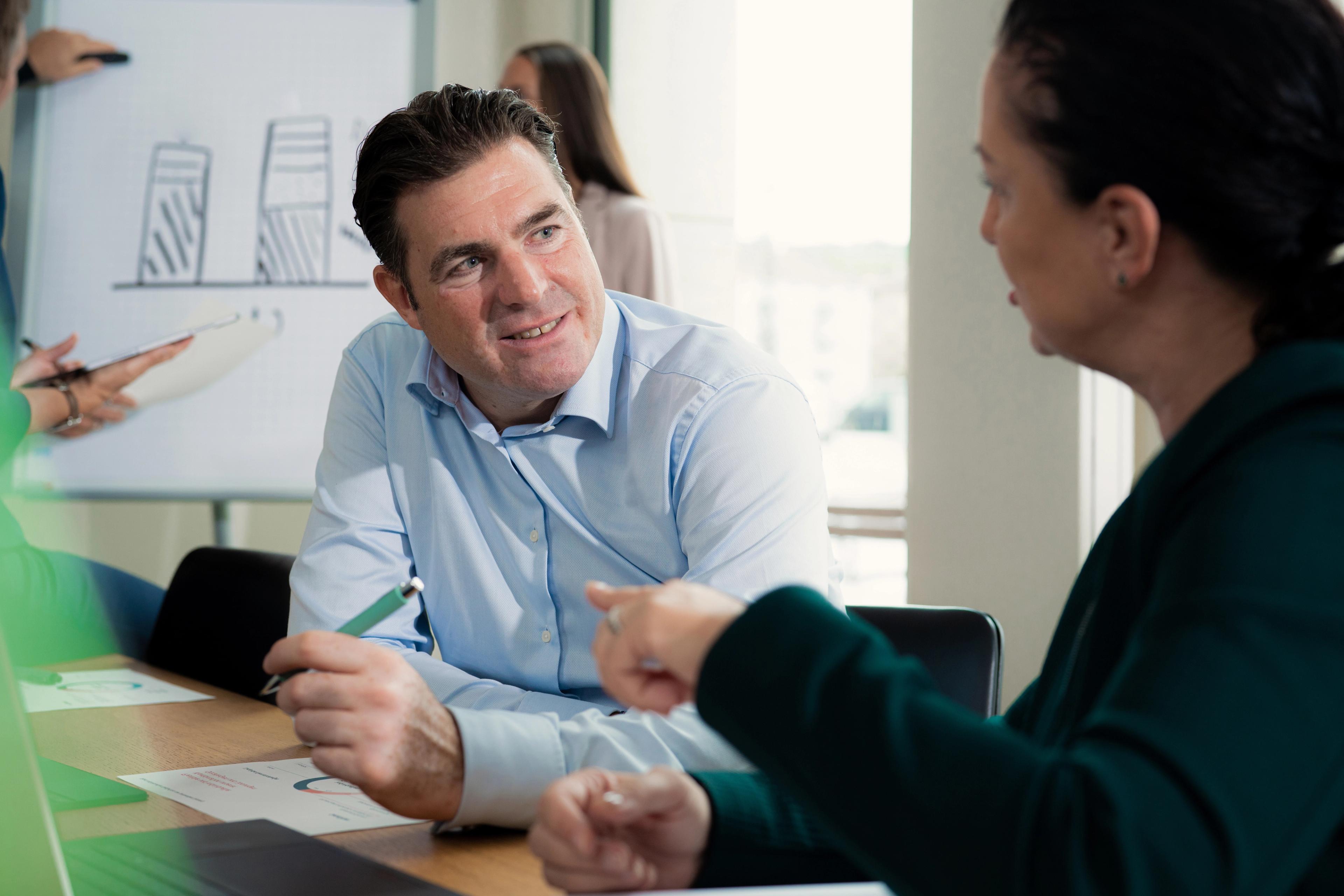 Mann und Frau diskutieren bei einem Meeting, im Hintergrund Flipchart mit Diagrammen