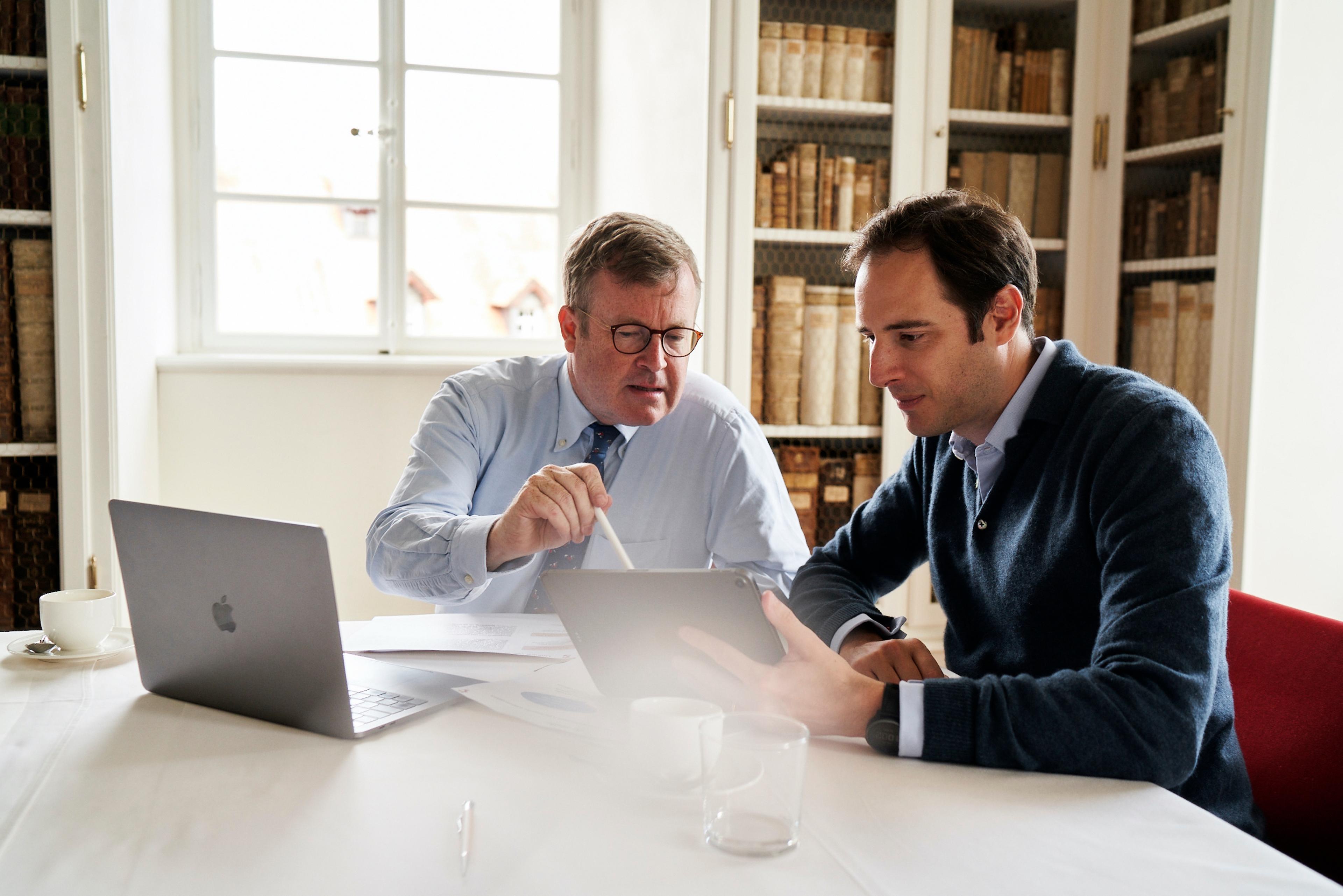 Ferdinand Fürst zu Castell-Castell und Otto Fürst zu Castell-Rüdenhausen sitzen an einem Tisch mit Laptop und Dokumenten, diskutieren konzentriert in einem Raum mit Bücherregalen.
