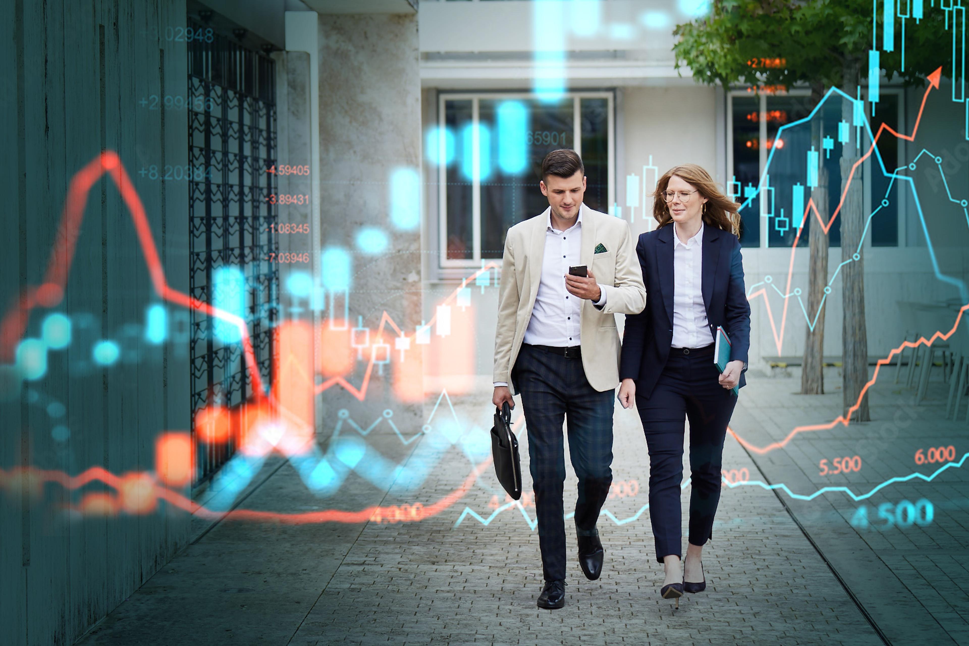 Zwei Geschäftsleute, ein Mann und eine Frau, gehen mit Akten und Smartphone durch eine Stadt, umgeben von digitalen Finanzdiagrammen