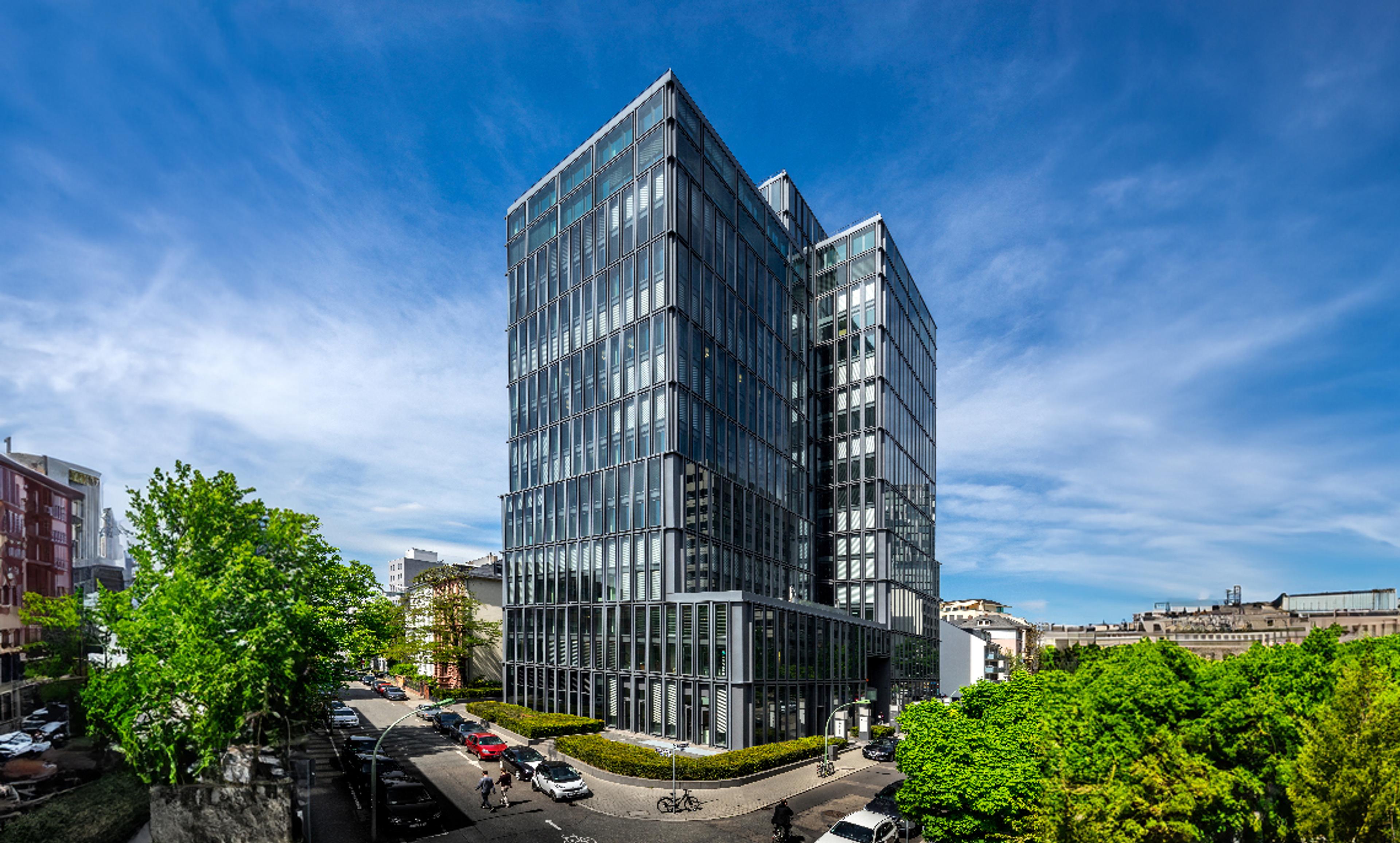 Modernes Bürogebäude mit Glasfassade in urbaner Umgebung bei blauem Himmel