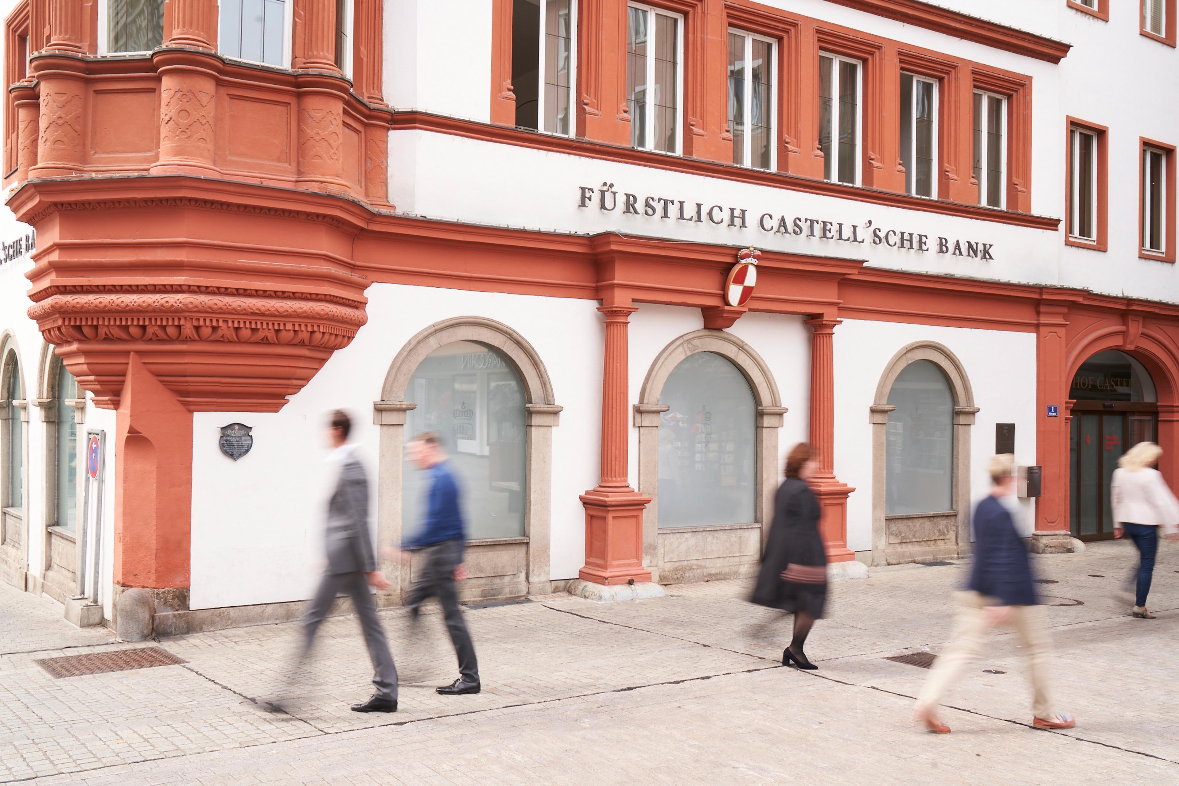 Gebäude der Fürstlich Castell'schen Bank mit roten Verzierungen und mehreren Passanten auf dem Gehweg