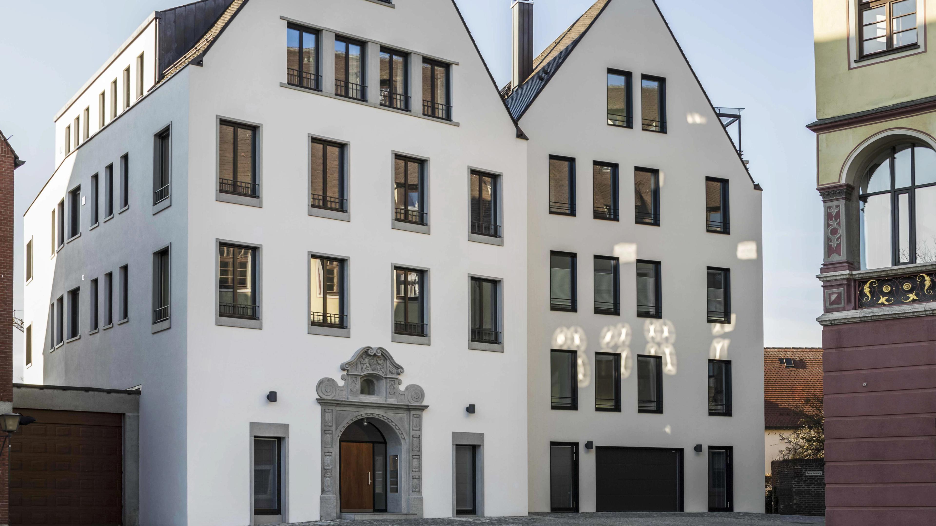 Modernes weißes Wohngebäude mit vielen Fenstern und einem verzierten Eingang in einer städtischen Umgebung