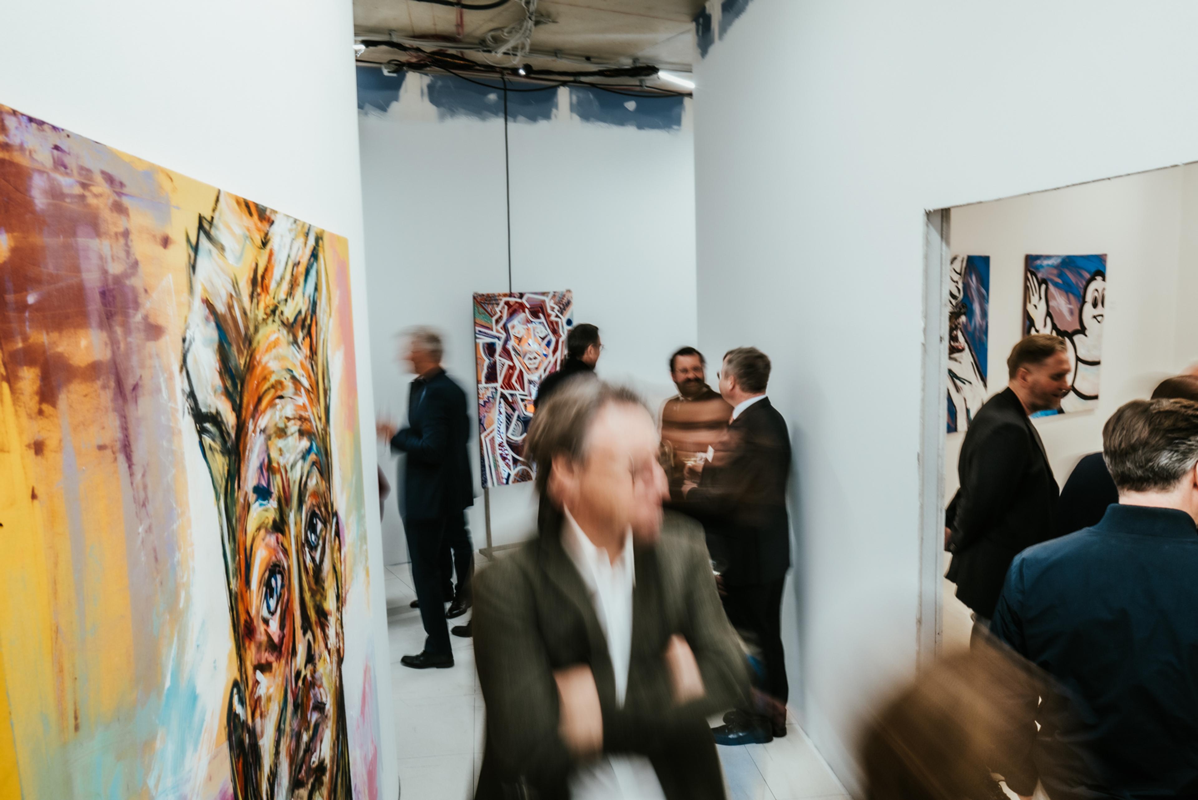 Menschen in formeller Kleidung in einer Galerie mit farbenfrohen, abstrakten Gemälden an den Wänden