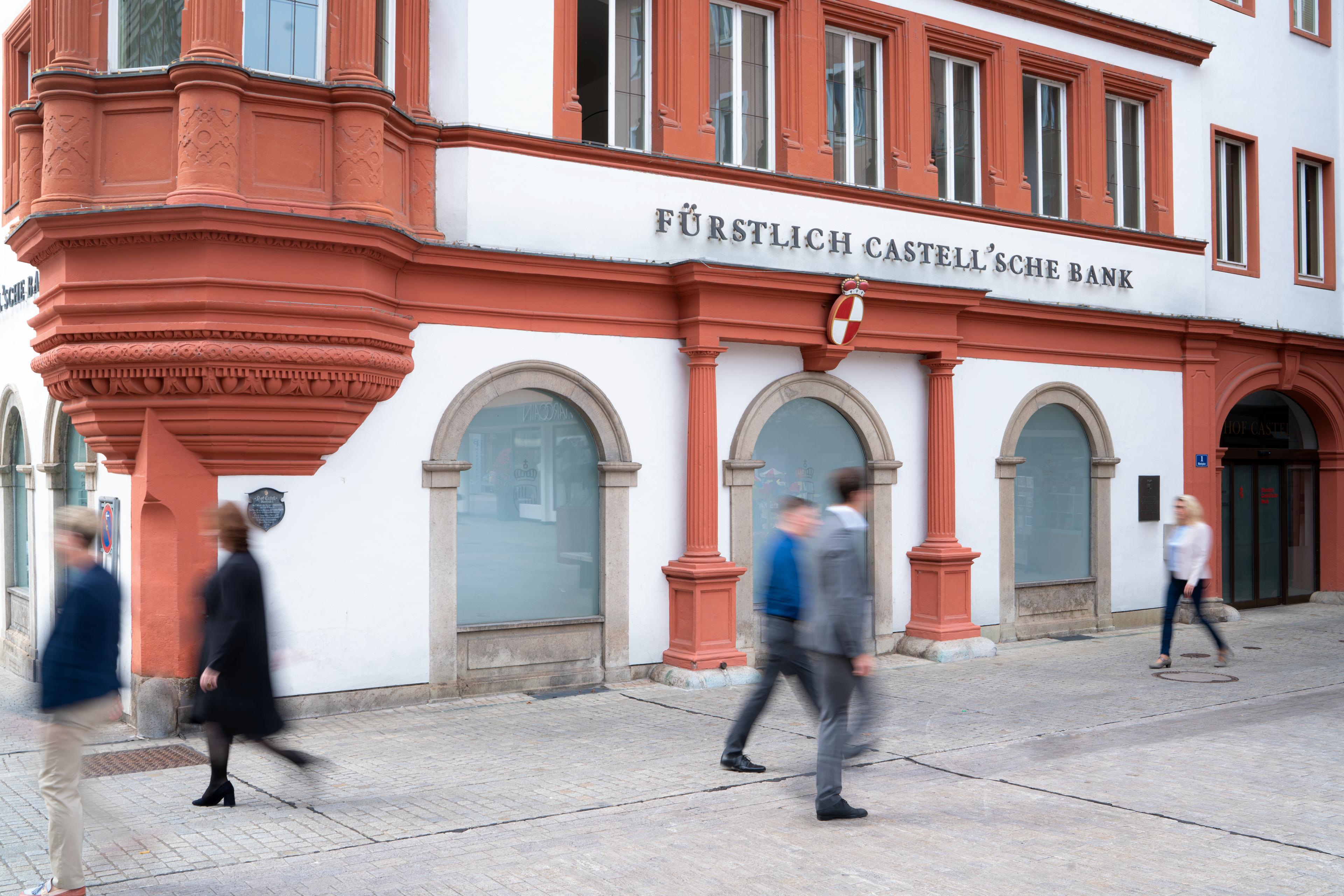 Gebäude der Fürstlich Castell'schen Bank mit roten Verzierungen und mehreren Passanten auf dem Gehweg