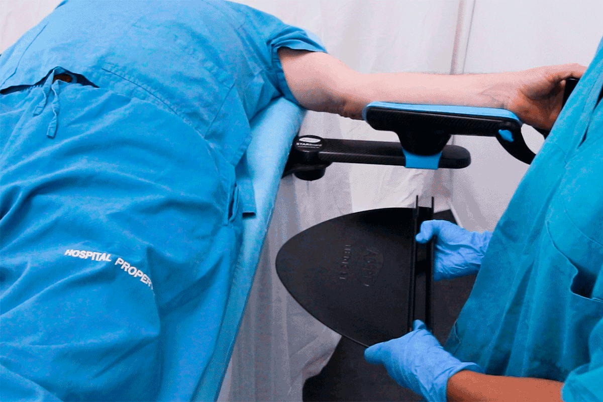 Patient's arm supported by a medical device, a gloved healthcare worker holds an instrument.
