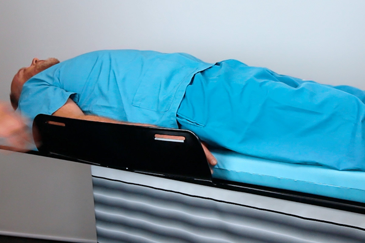 Patient in blue scrubs lying on a medical table with arms in supports.