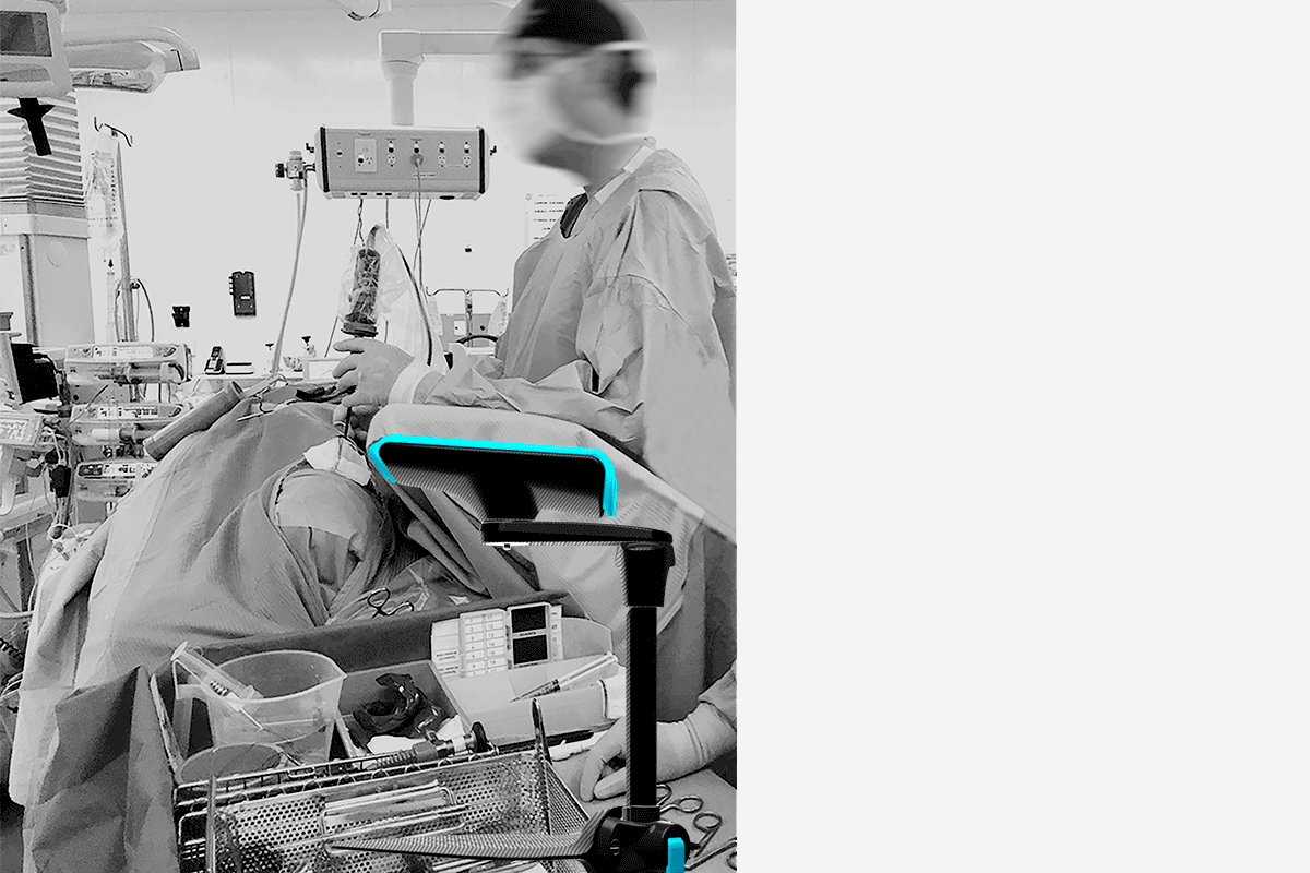 Surgeon operating on a draped patient in a grayscale room, with a blue-highlighted medical device.