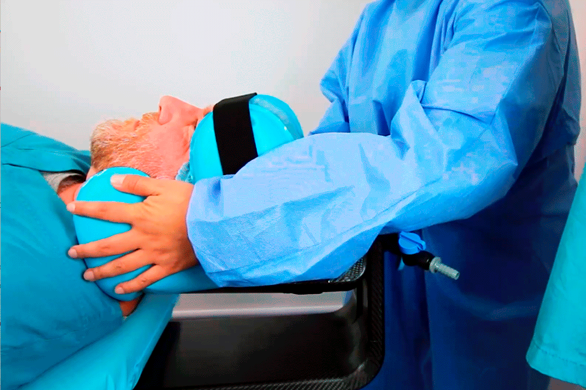 A medical professional uses a blue head and neck support device on a patient.