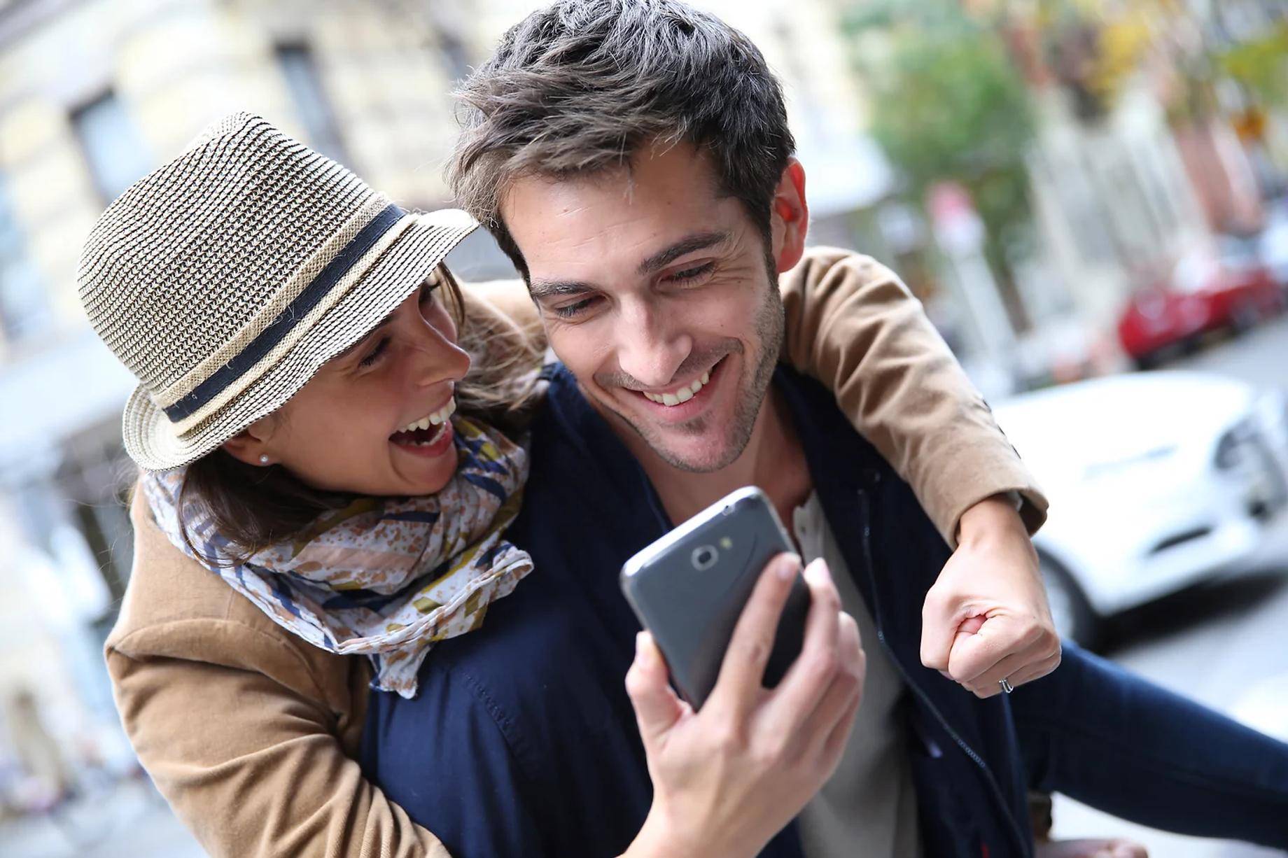 A couple in playful embrace both looking at a smartphone screen