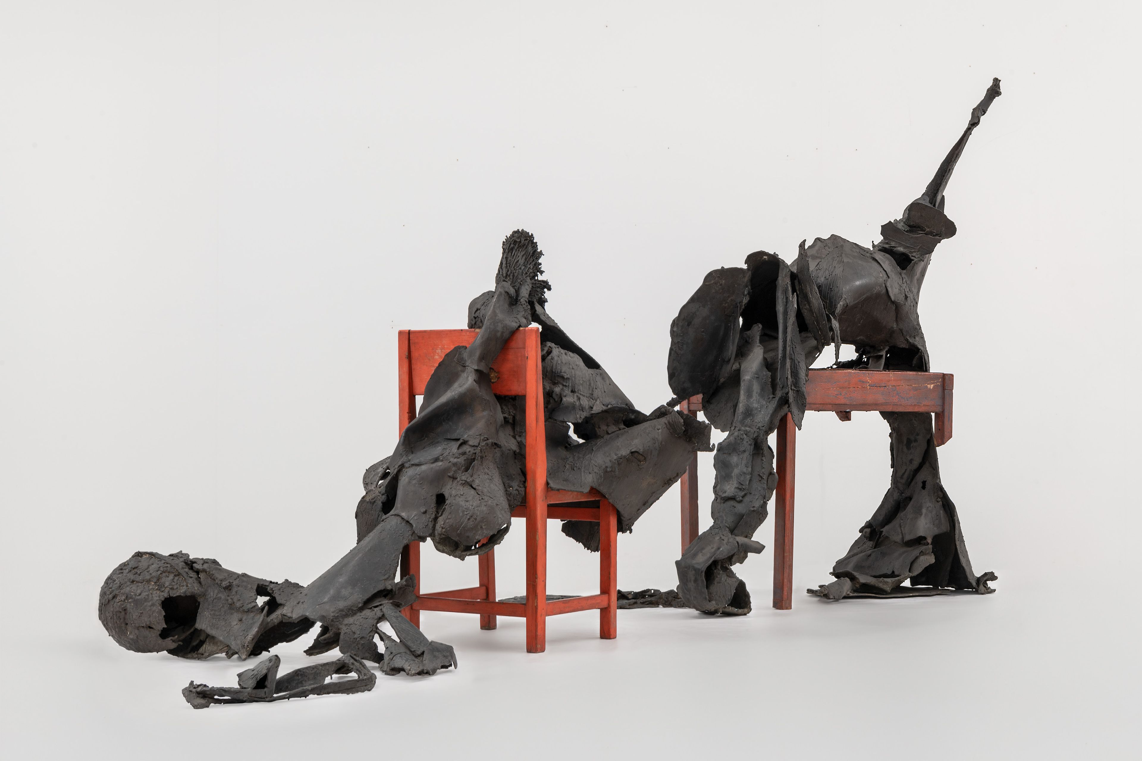 Wessel Couzijn, _Rendez-vous van tafel en stoel_, 1964-1965 Bronzen vormen die lijken op een mens liggend op een halve tafel en een stoel