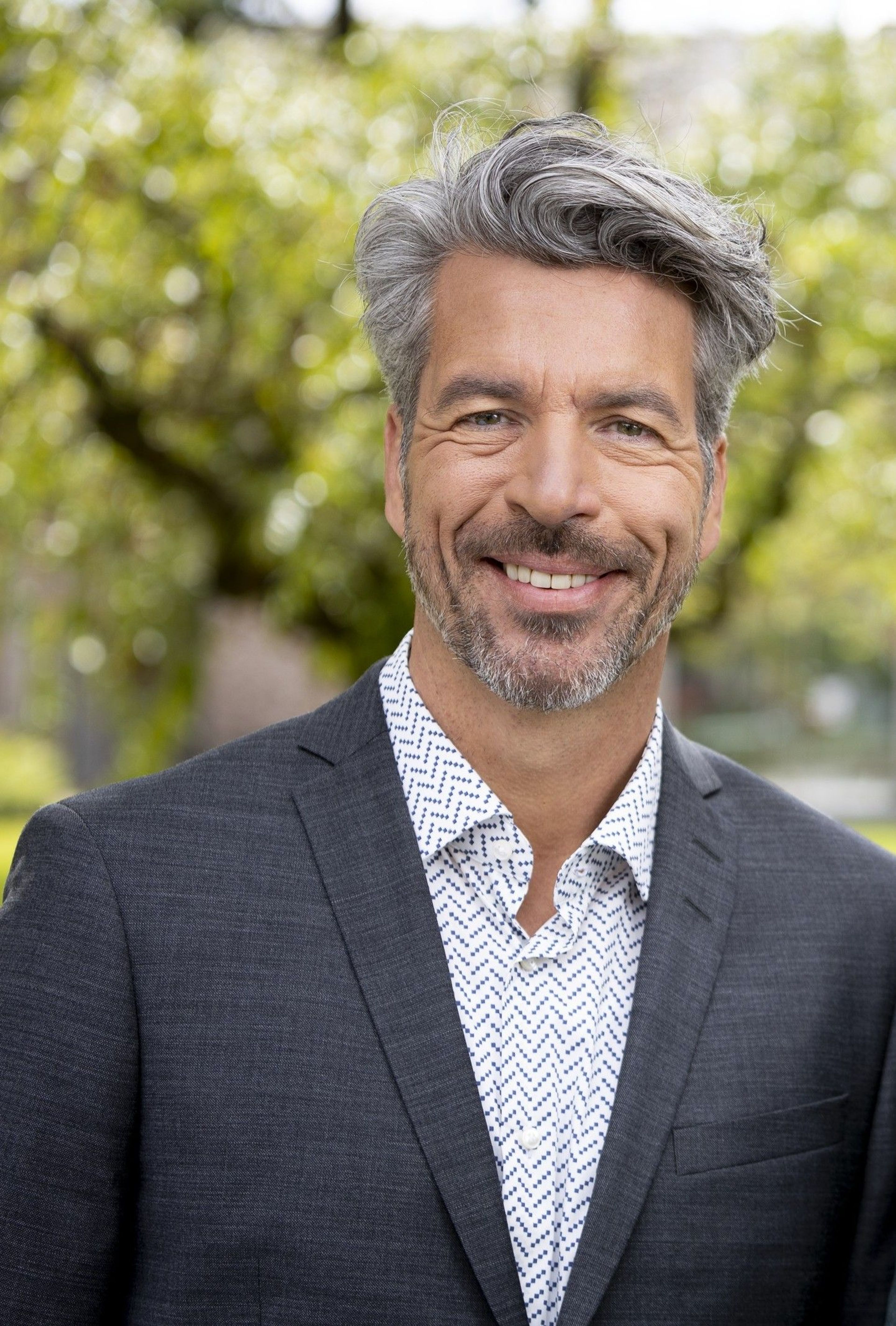 Portretfoto van een man met grijs haar, gekleed in een donkergrijs colbert en een wit overhemd
