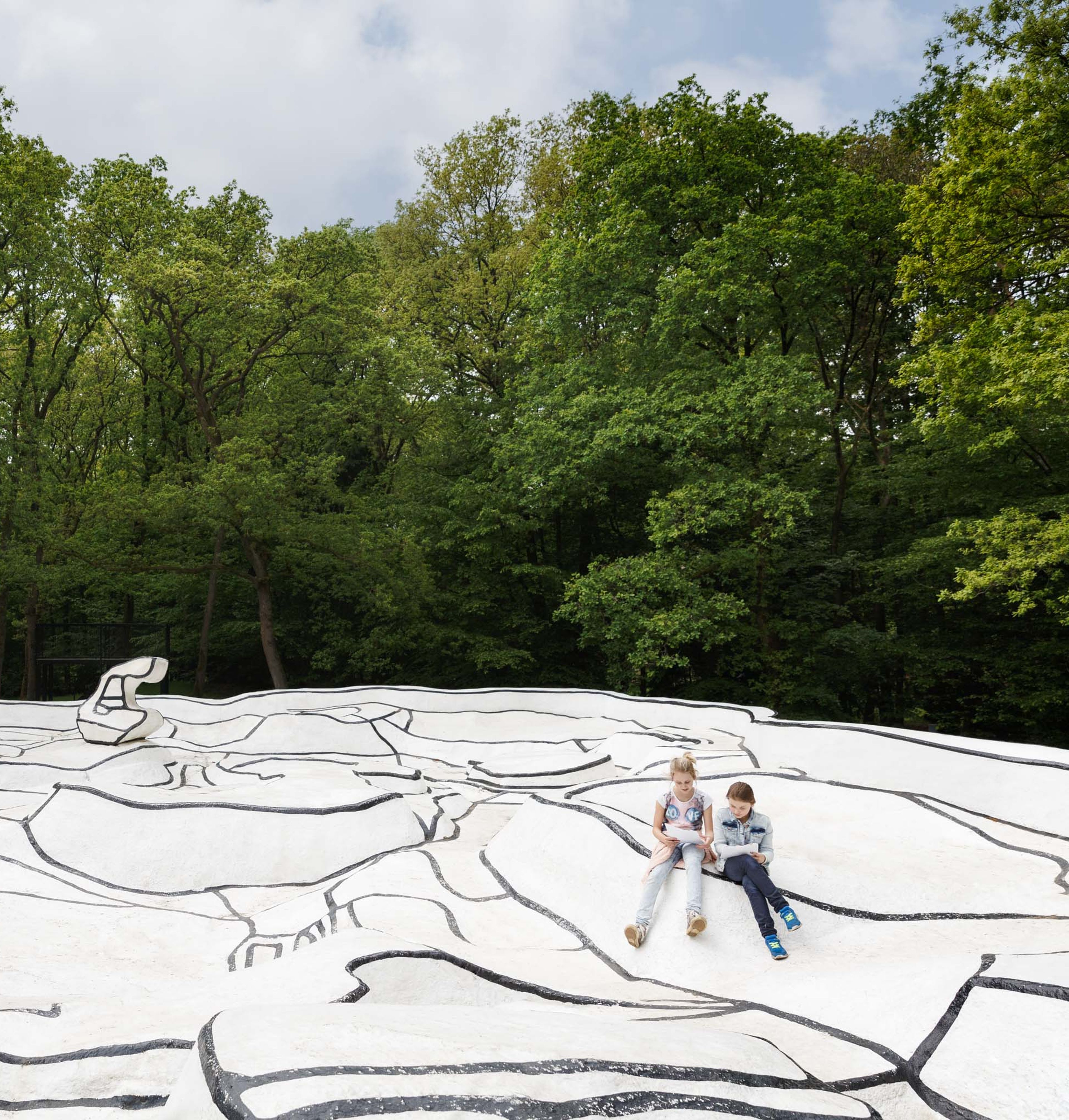 Twee kinderen zitten op het kunstwerk 'Jardin d'email', een zwart-witte ondergrond in een bos