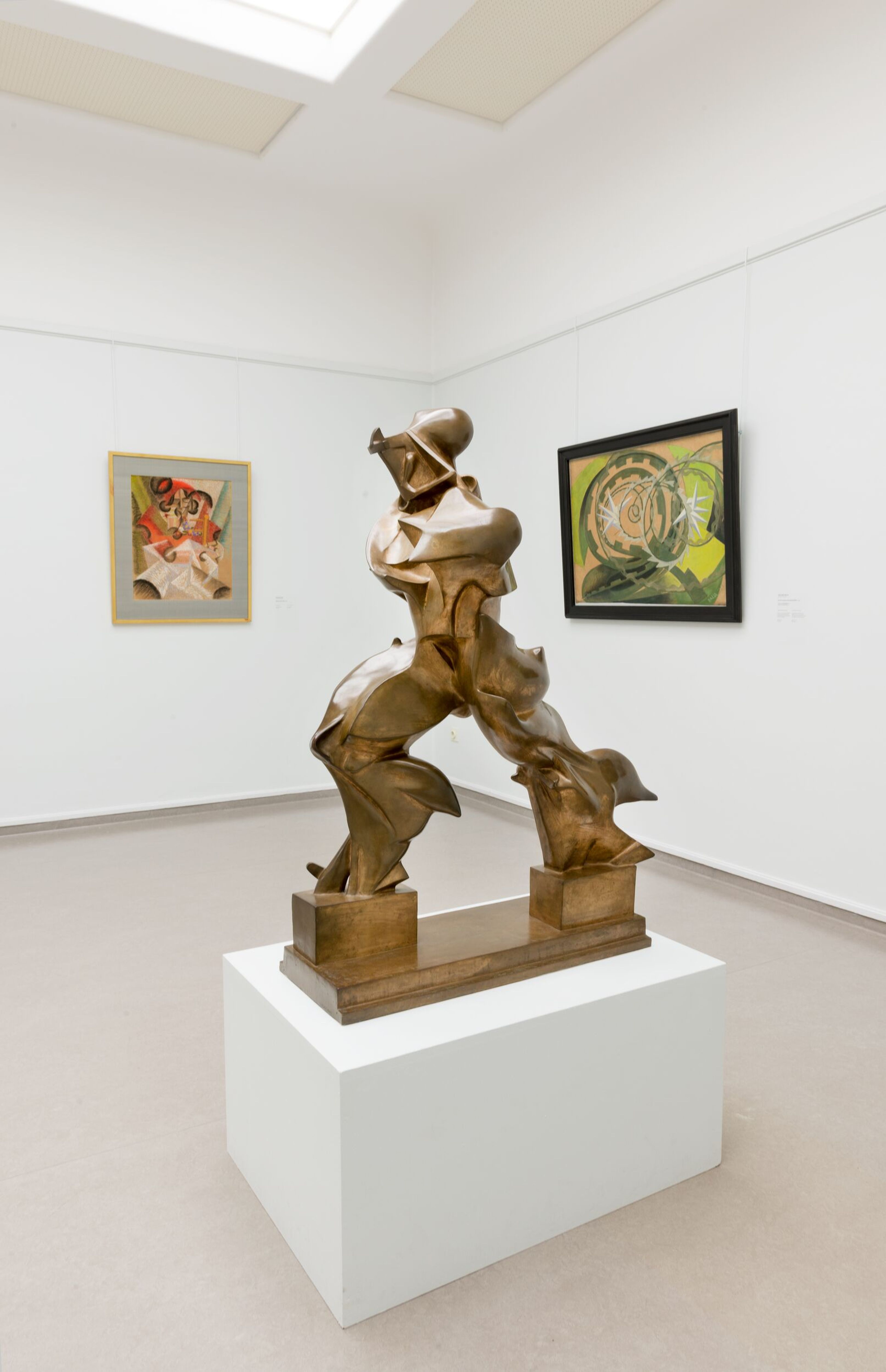 Bronze abstract sculpture of a human figure in a dynamic, forward-leaning pose. The sculpture is composed of angular, fragmented forms and stands on a rectangular base against a neutral background.