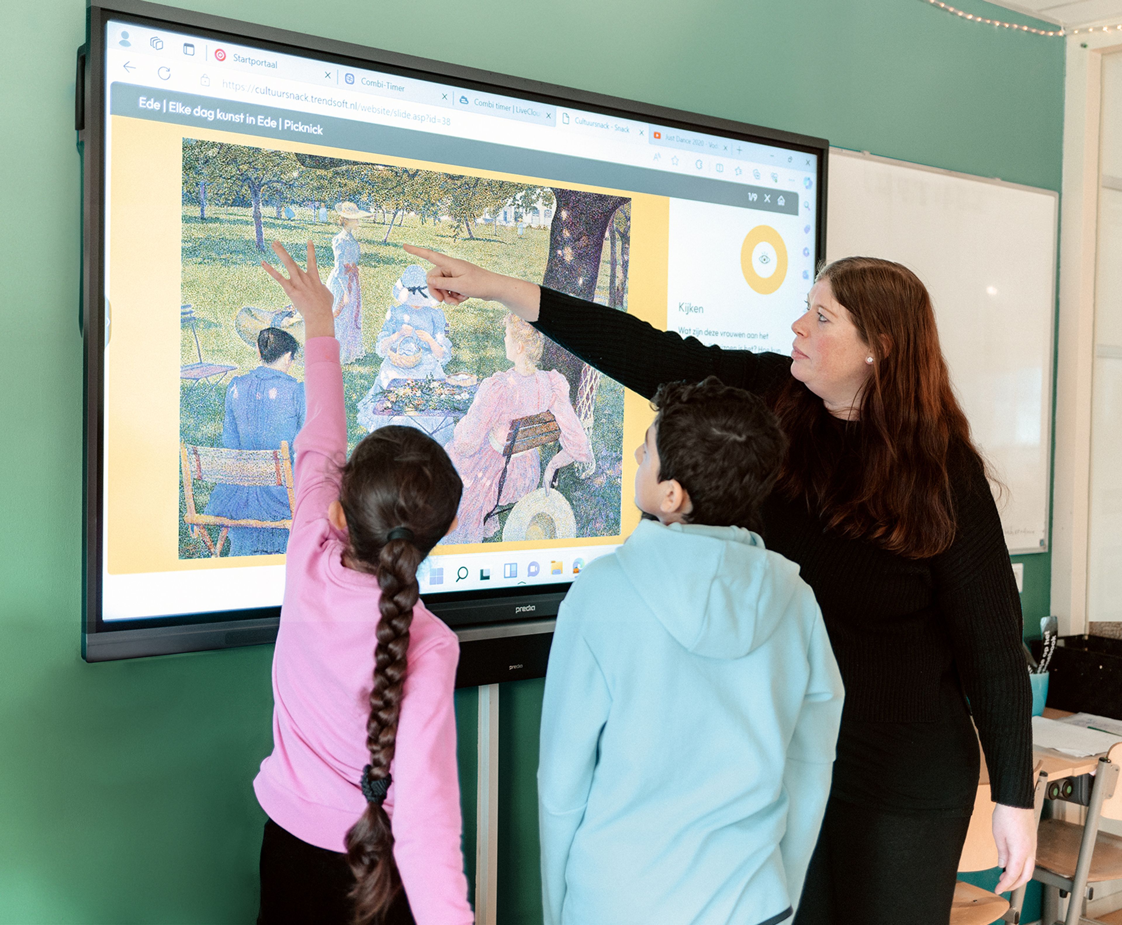 Foto van een klaslokaal met een docent en twee kinderen die naar een digitaal scherm kijken waarop een schilderij wordt getoond. Docent wijst naar details in het kunstwerk terwijl kinderen aandachtig volgen, wat wijst op een educatieve kunstles.