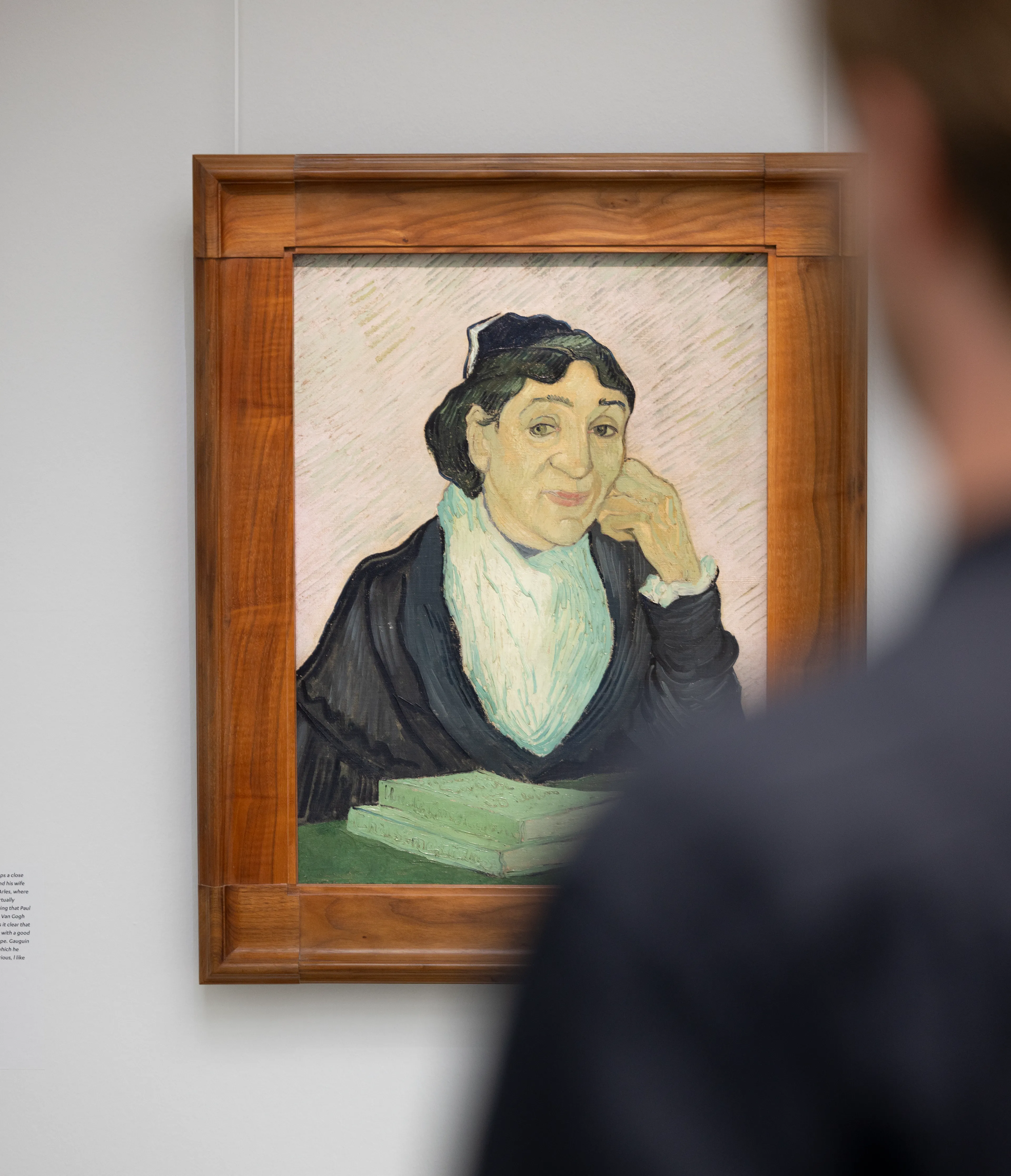 Foto van een persoon die naar een schilderij kijkt . Schilderij toont een vrouw met donkere kleding en een witte sjaal, omlijst door een houten lijst, met een boek op tafel voor haar.