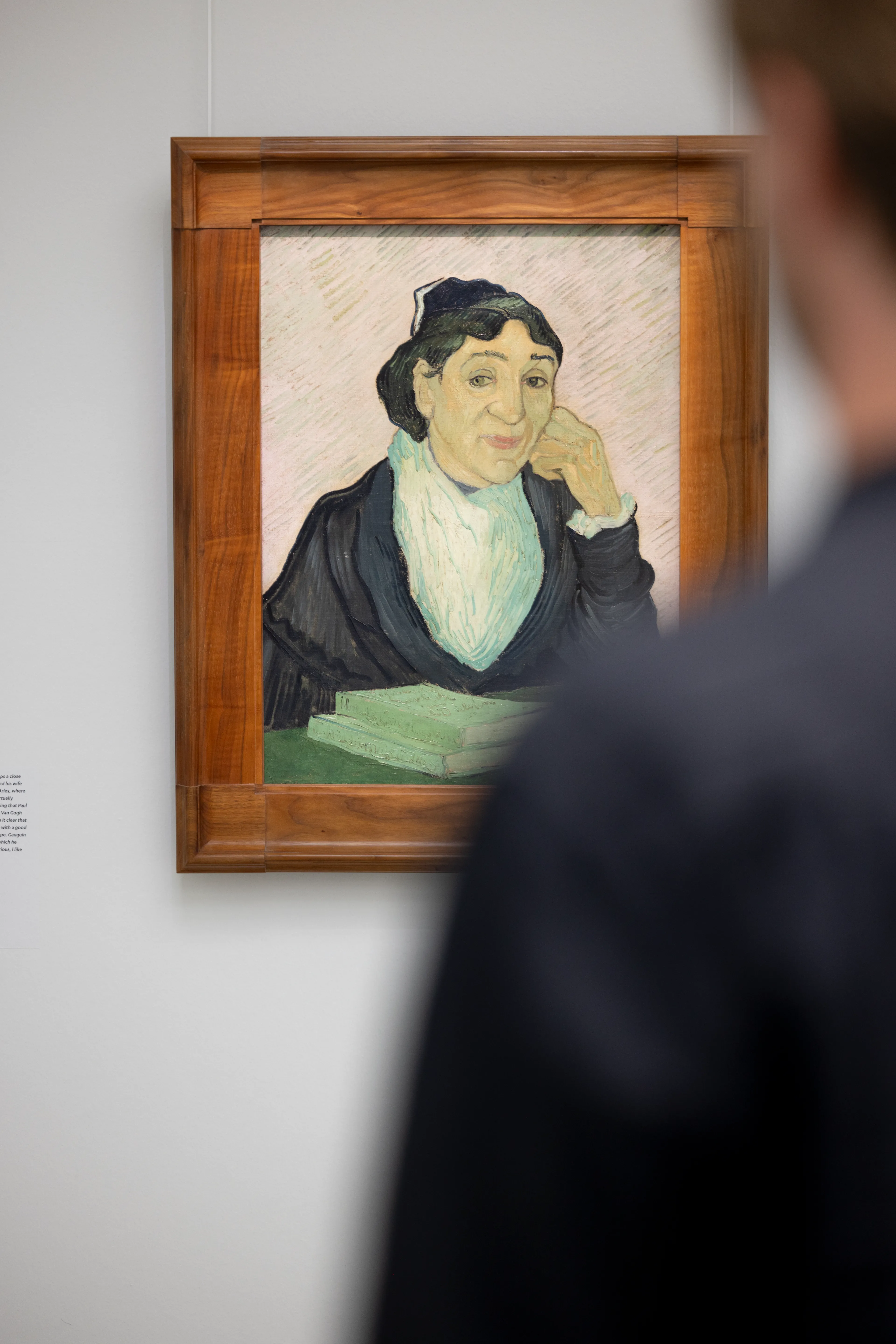 Foto van een persoon die naar een schilderij kijkt . Schilderij toont een vrouw met donkere kleding en een witte sjaal, omlijst door een houten lijst, met een boek op tafel voor haar.