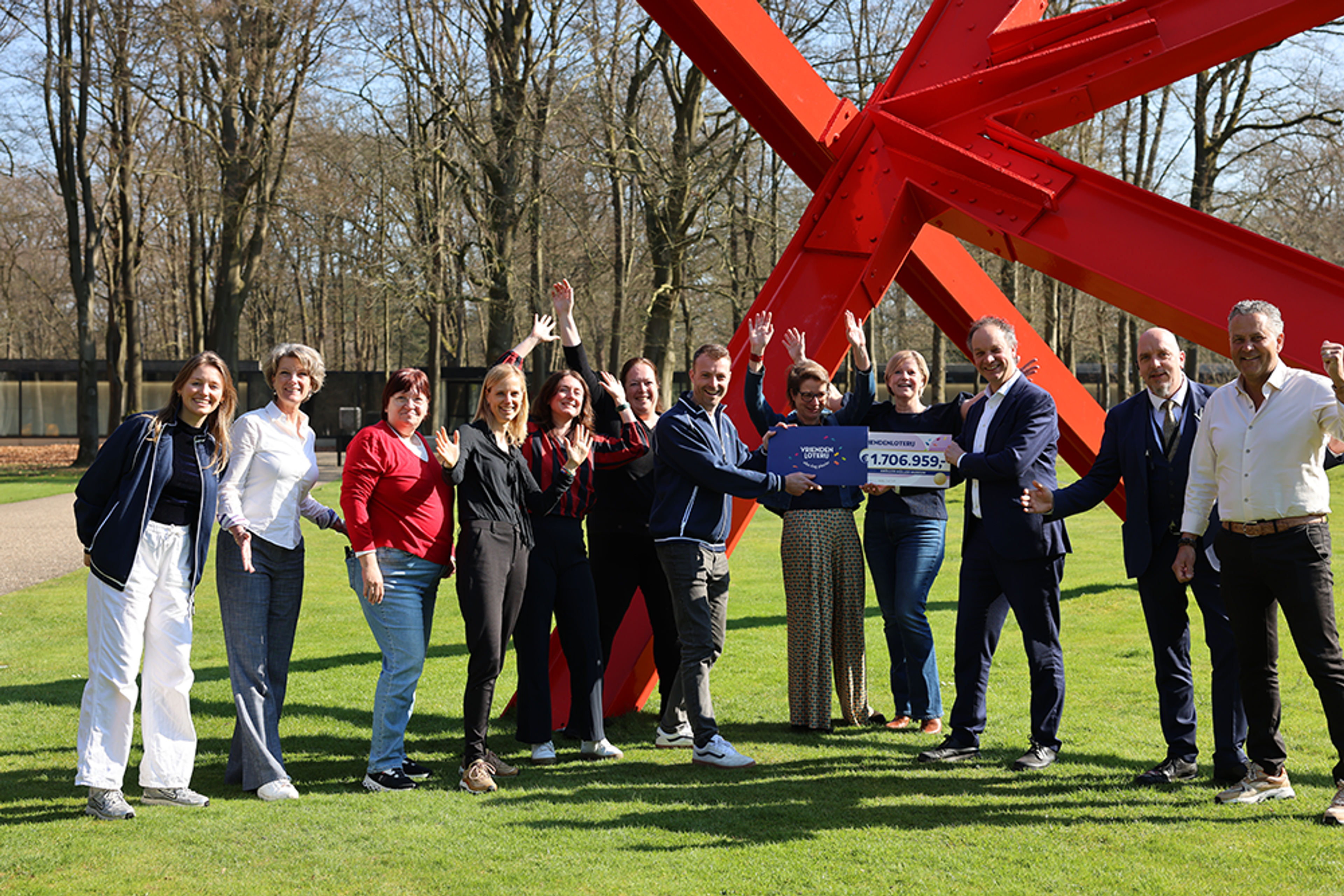 Medewerkers ontvangen cheque van de VriendenLoterij, voor het museum bij een groot rood kunstwerk