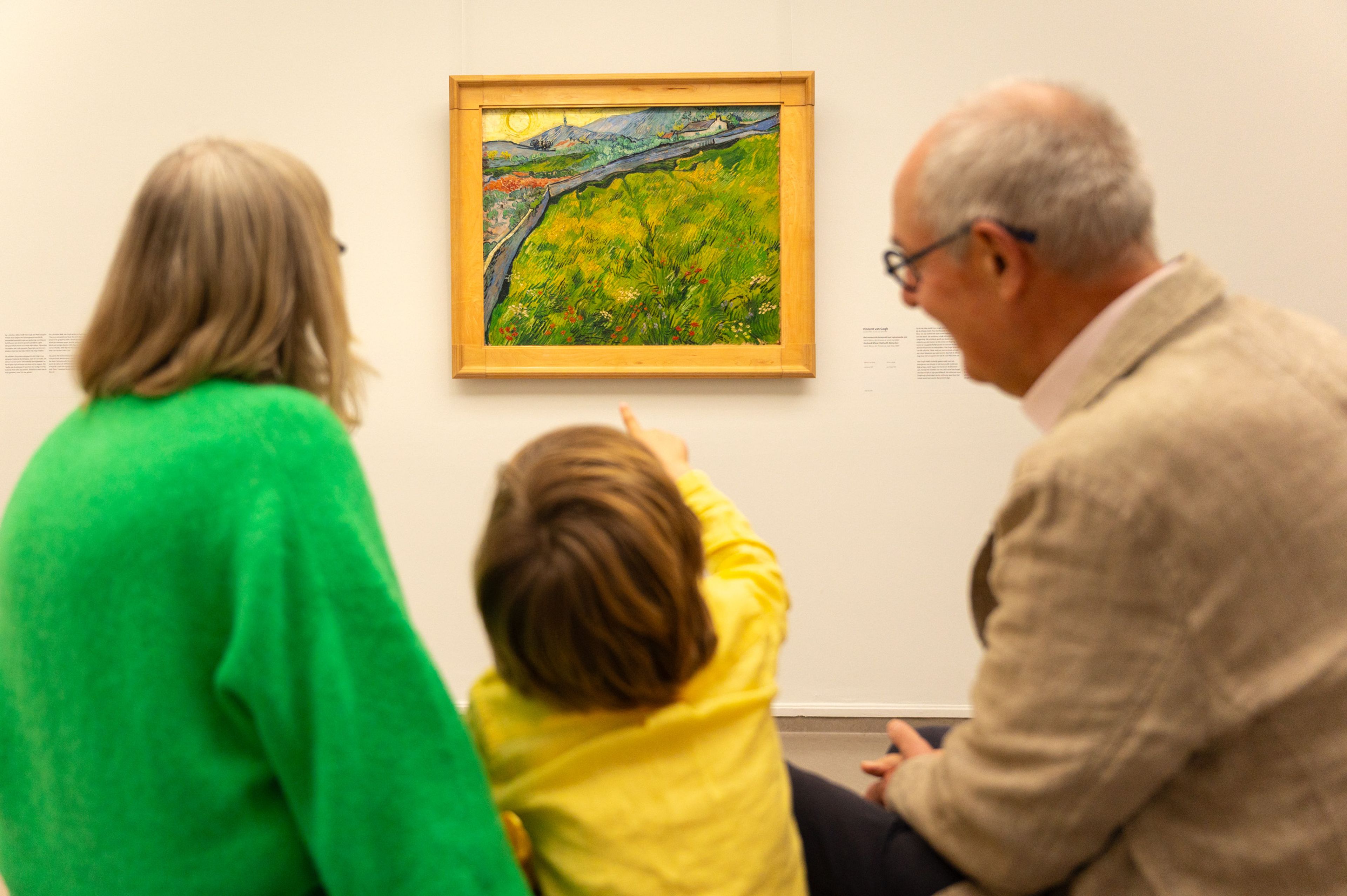Twee volwassenen en een kind zitten voor een schilderij van Vincent van Gogh. Het kind wijst naar het schilderij.