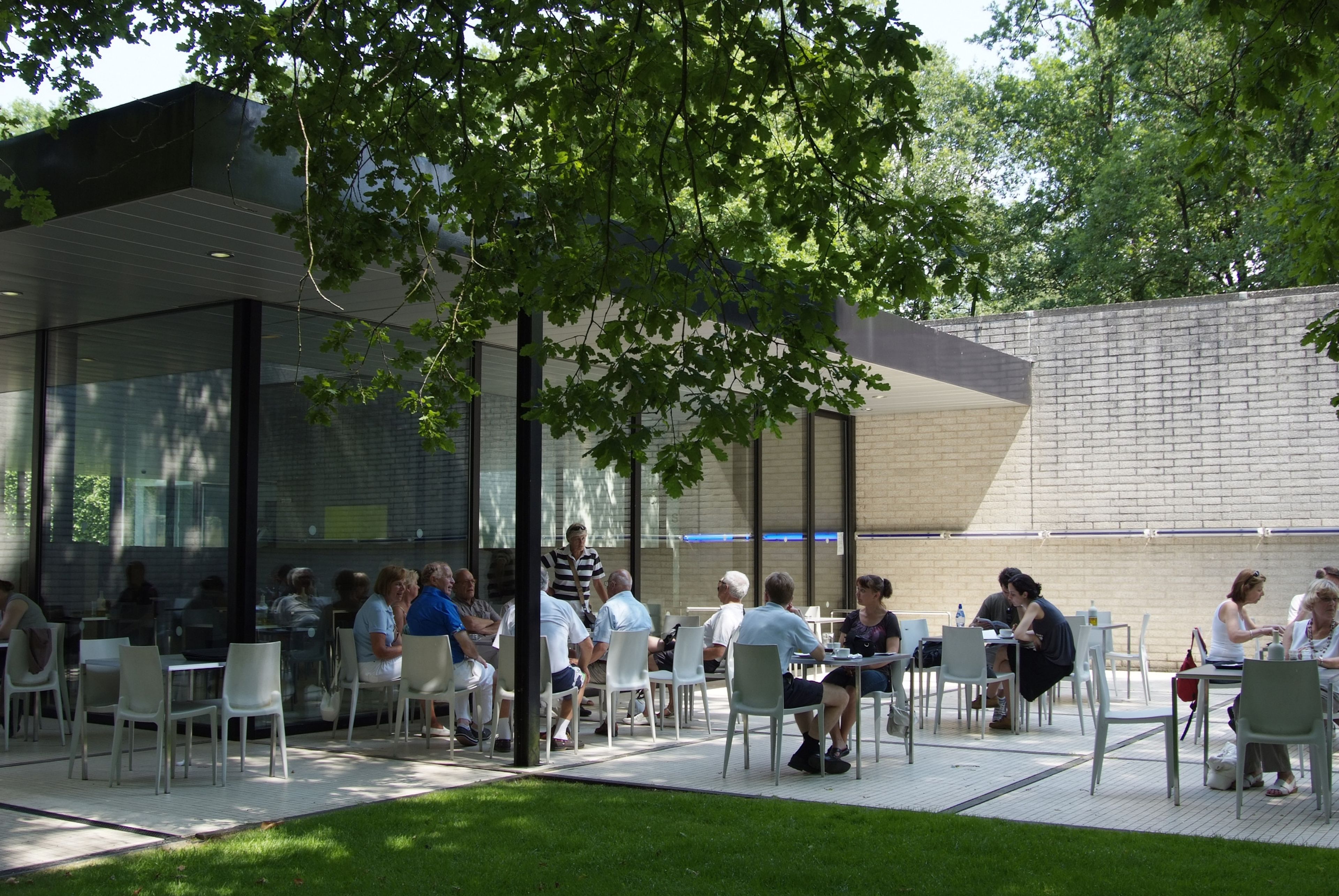 Bezoekers buiten op het terras van museumrestaurant MJ, onder een groene boom
