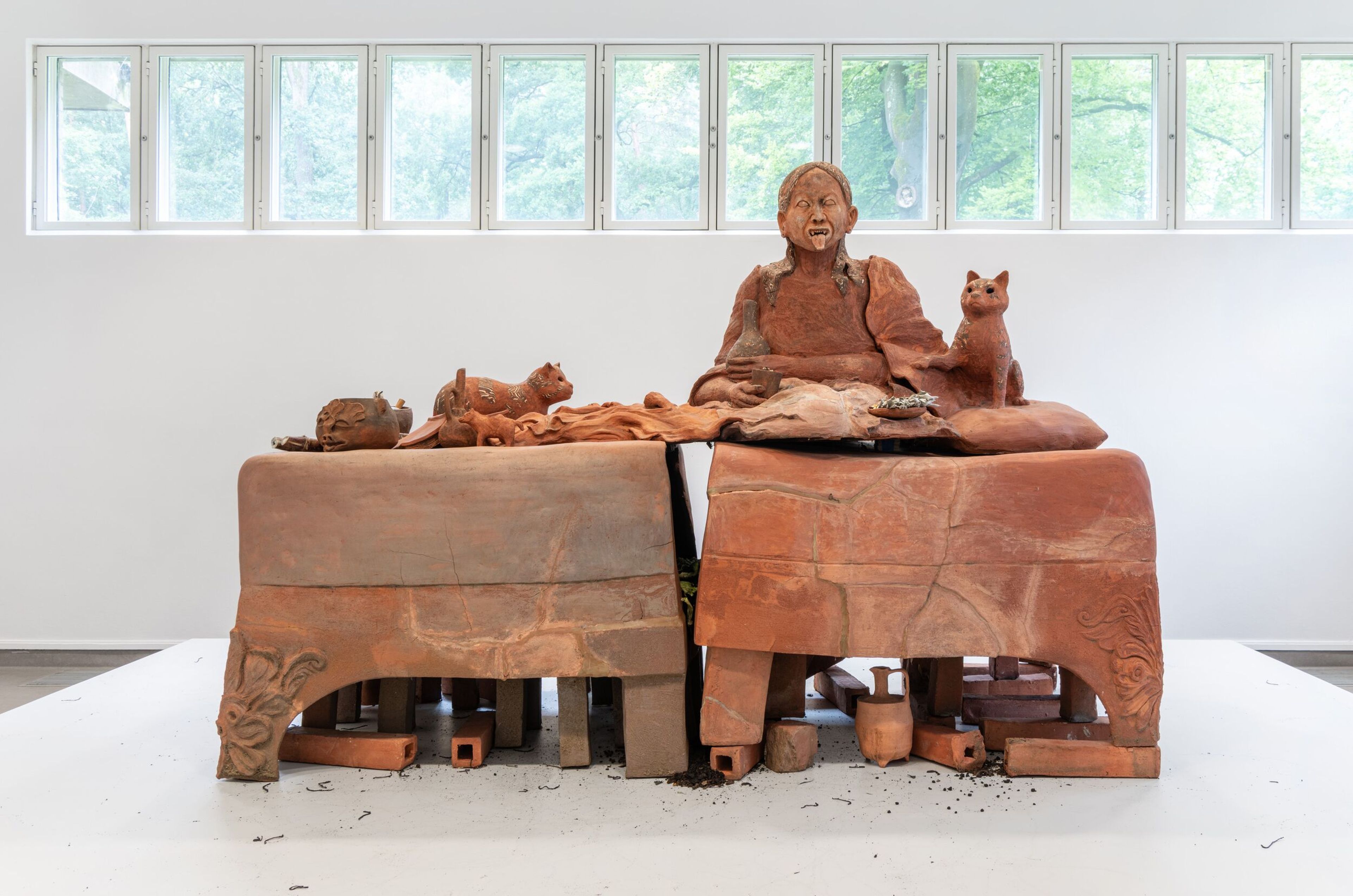 Candice Lin’, _Future Sarcophagus_, 2020 Foto van een keramisch kunstwerk bestaande uit een zittend mensfiguur met dieren op een grote, gebroken bank