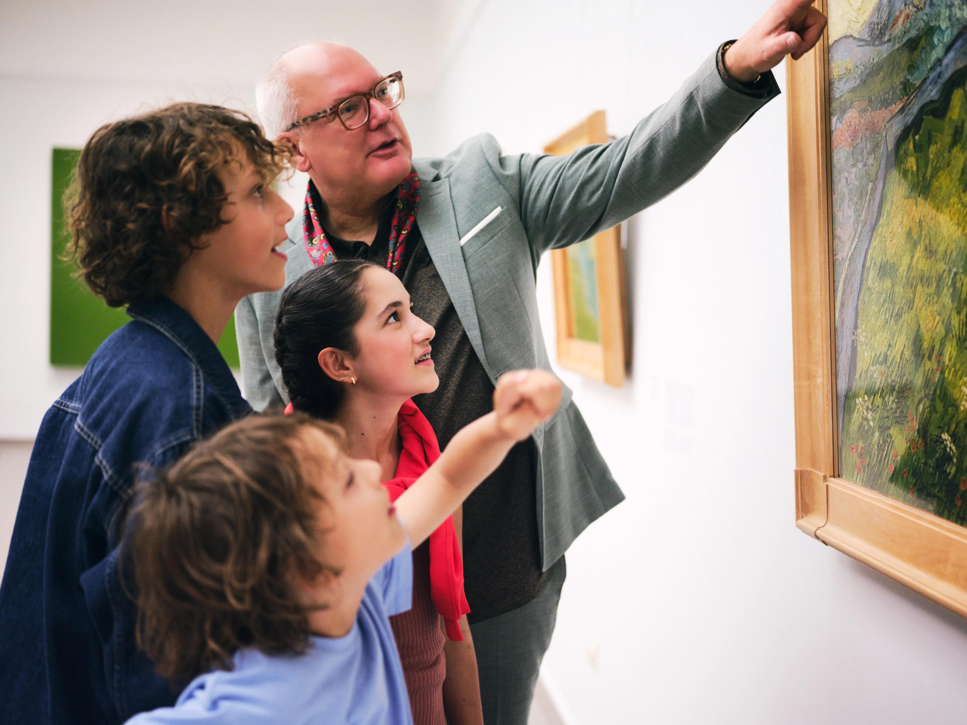 Man looking at a painting in a museum gallery together with three children of different ages.