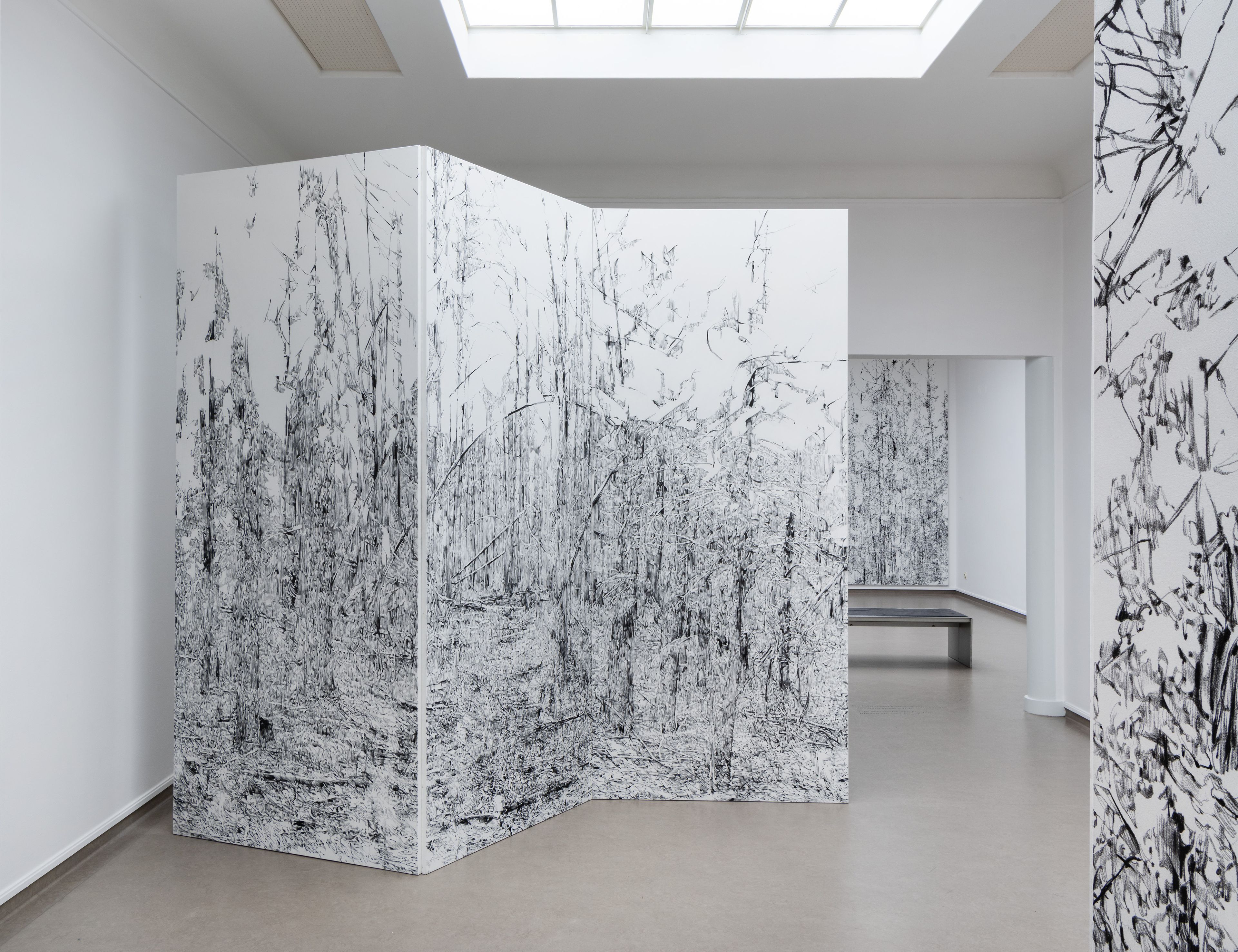 Foto van een kunstinstallatie in een witte ruimte met grote panelen bedrukt met gedetailleerde zwart-witte boslandschappen.
