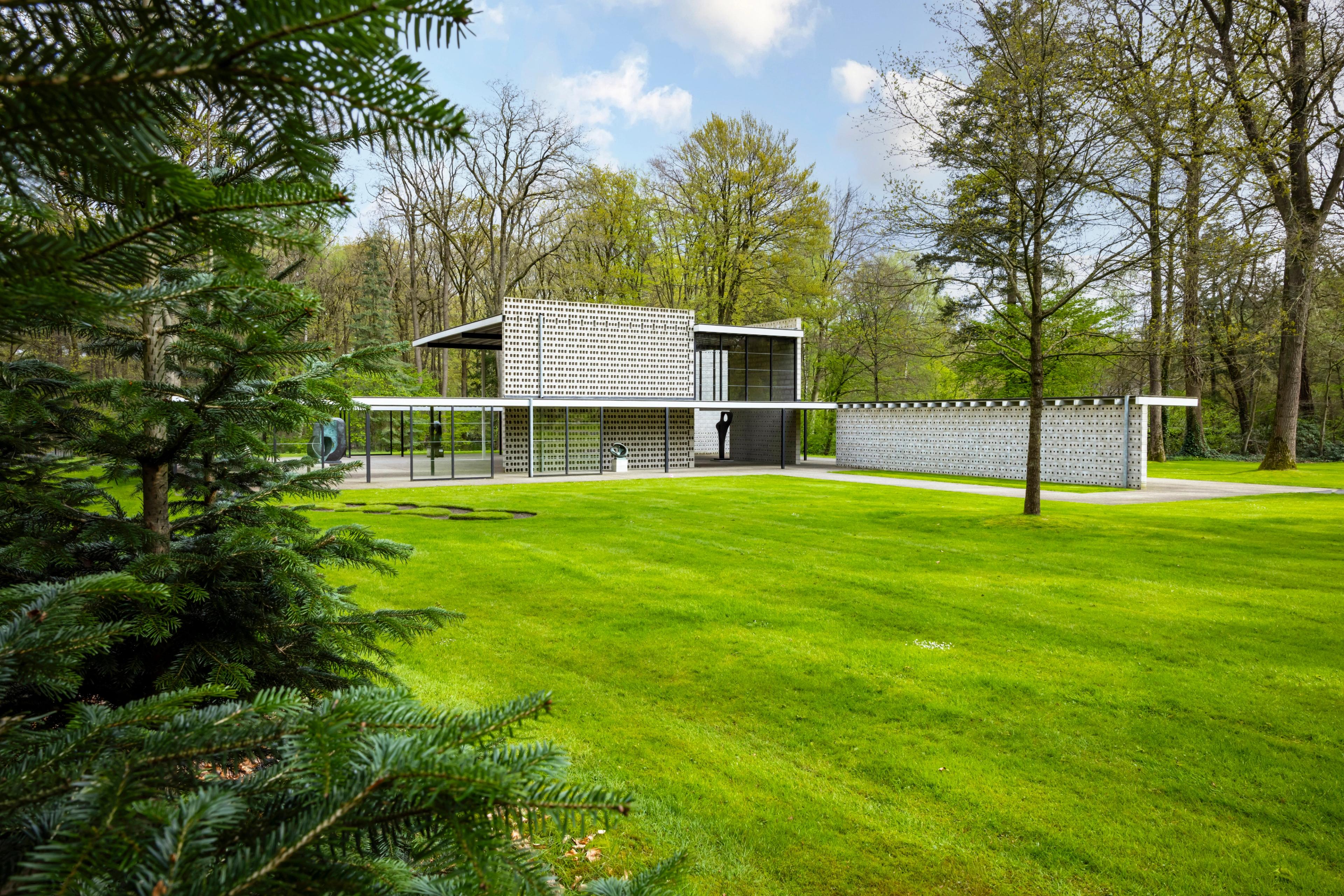 Gerrit Rietveld, Rietveldpaviljoen, 1964-1965 (herbouwd 2010) Foto van modern gebouw met strakke lijnen en grote glaspartijen, omgeven door een groene tuin met gras en bomen.