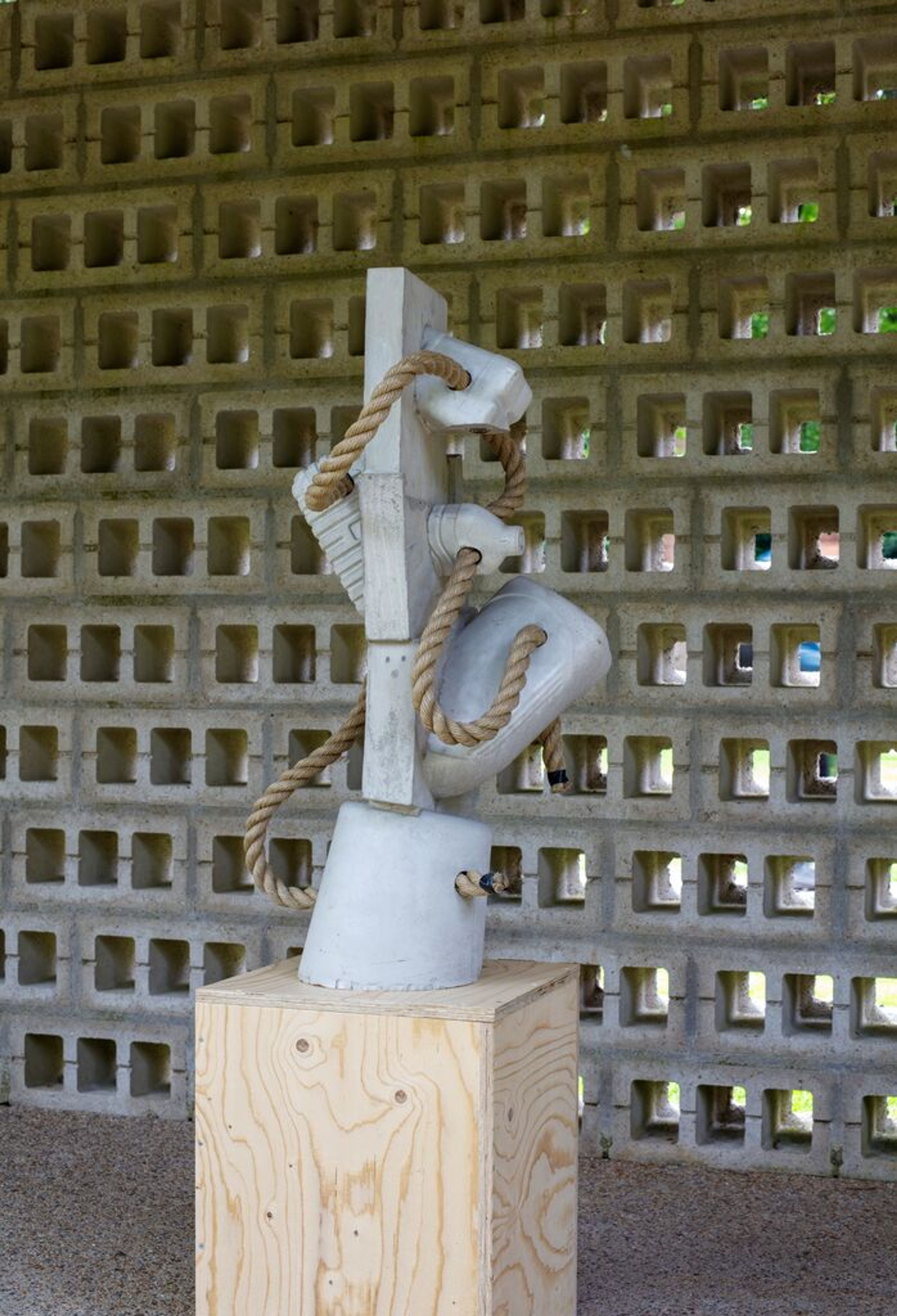 Ruud Kuijer, _Zonder titel_ (nr. 393), 2016, foto: Rob Versluys Foto van een beeld in lichtgrijs beton met touwen tegen een achtergrond van een opengewerkte muur. De vormen zijn speels, het touw is door het beeld heen gehaald