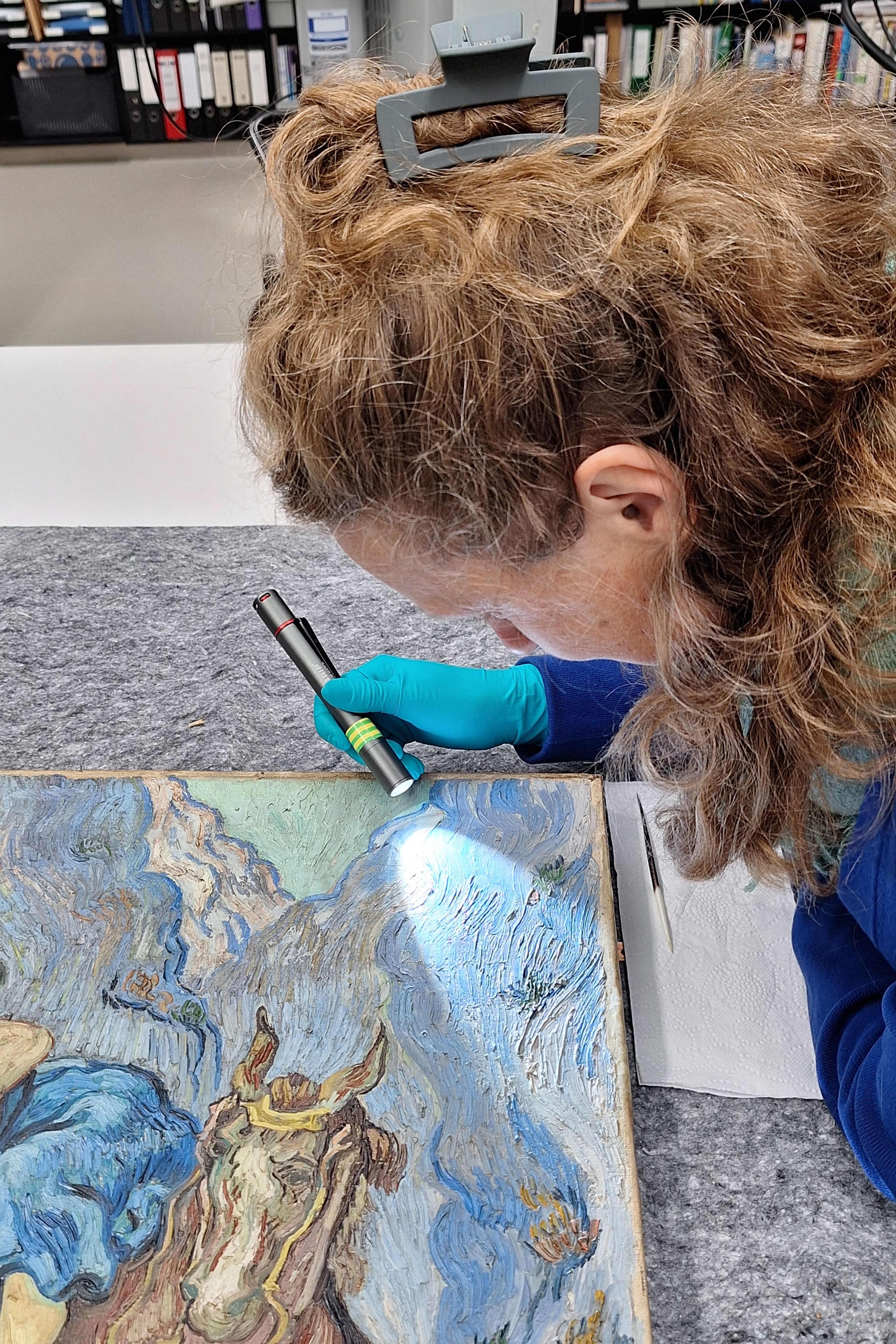 Foto van iemand die op een atelier aandachtig met een zaklamp kijkt naar een schilderij (Van Gogh)