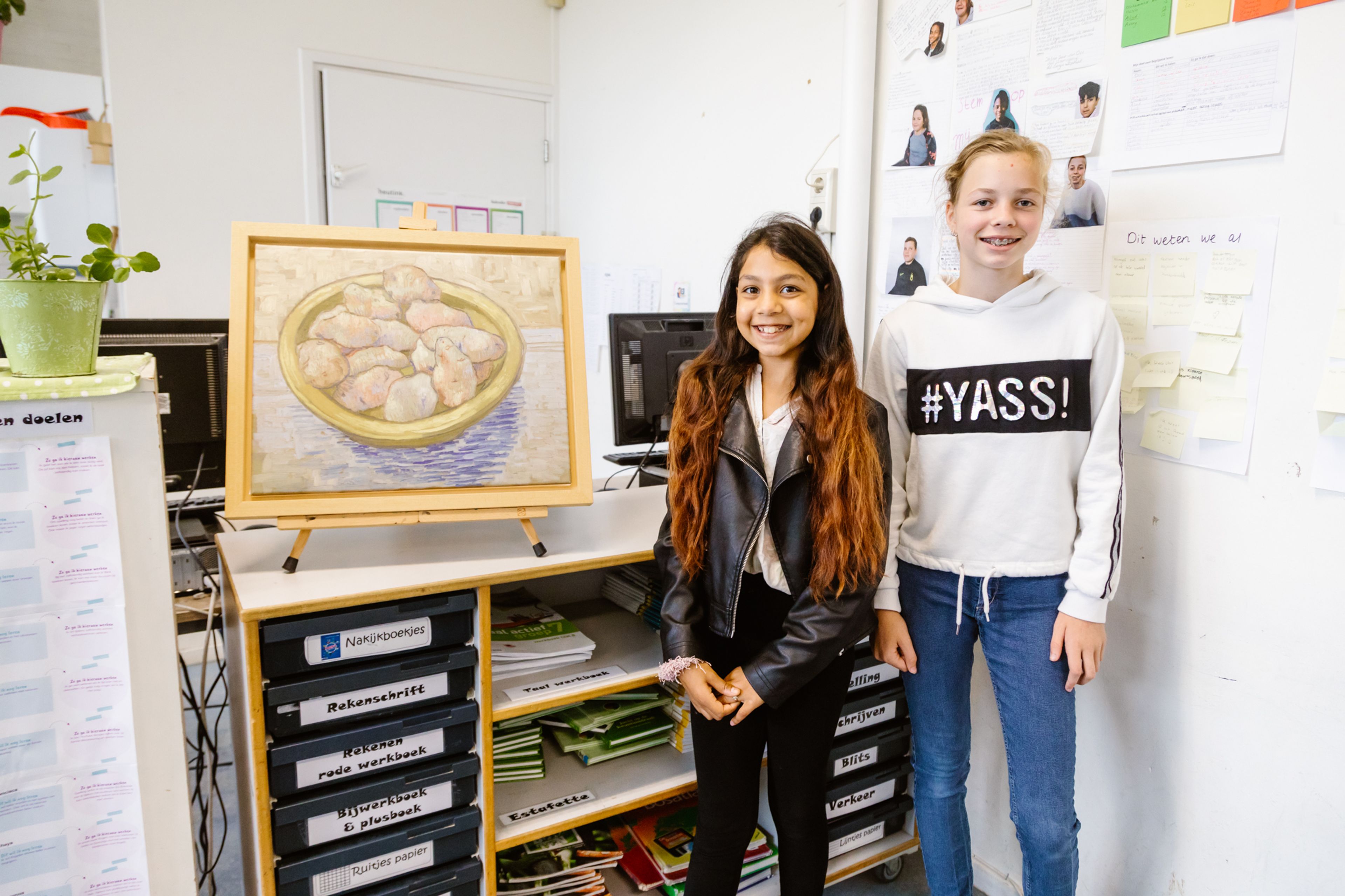 Twee scholieren in een klaslokaal. Ze staan naast een schildersezel met een reproductie van een schilderij van Vincent van Gogh
