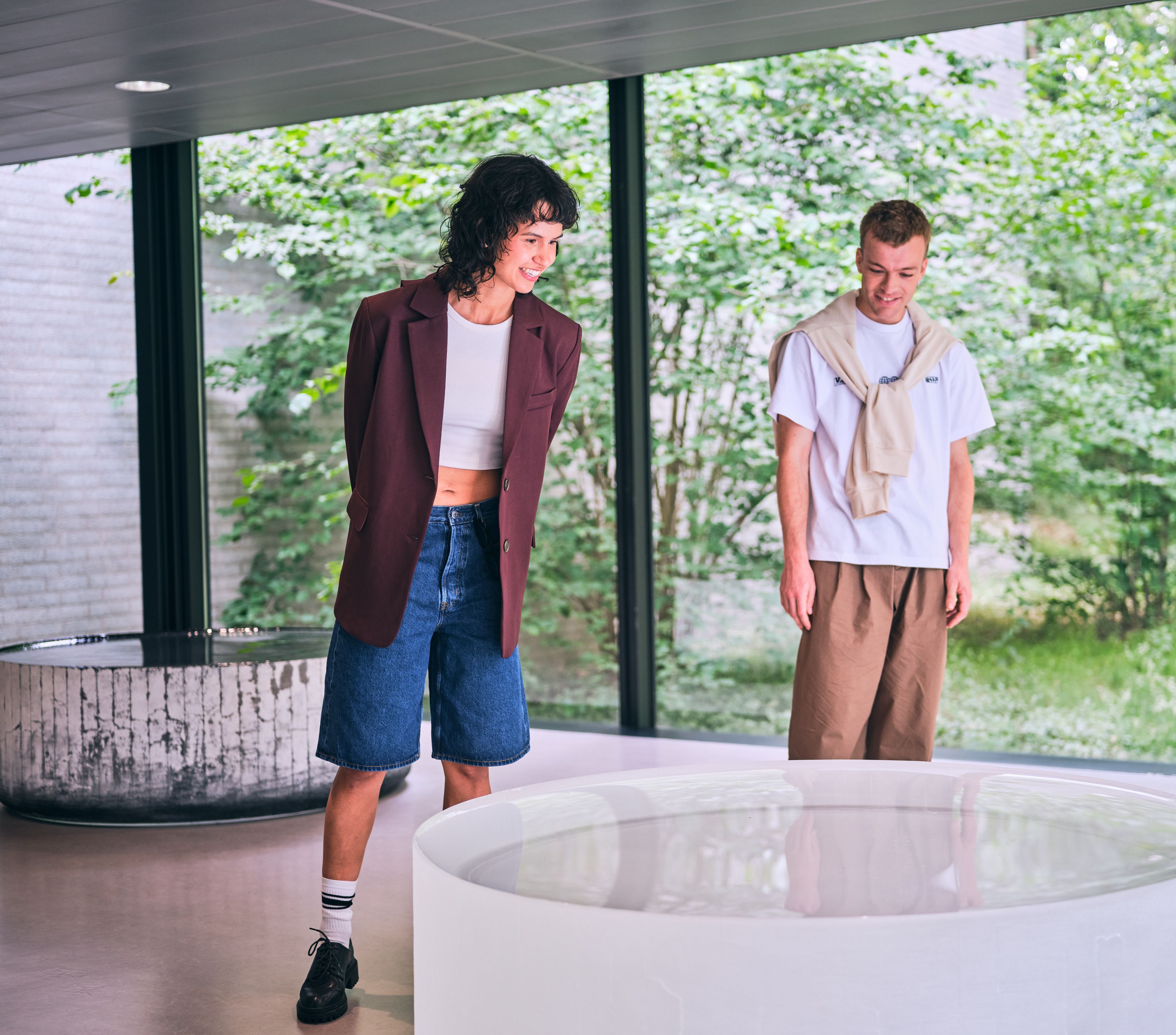 Twee bezoekers in een ruimte met uitzicht op groen, bij het kunstwerk 'Opposites of White' van Roni Horn