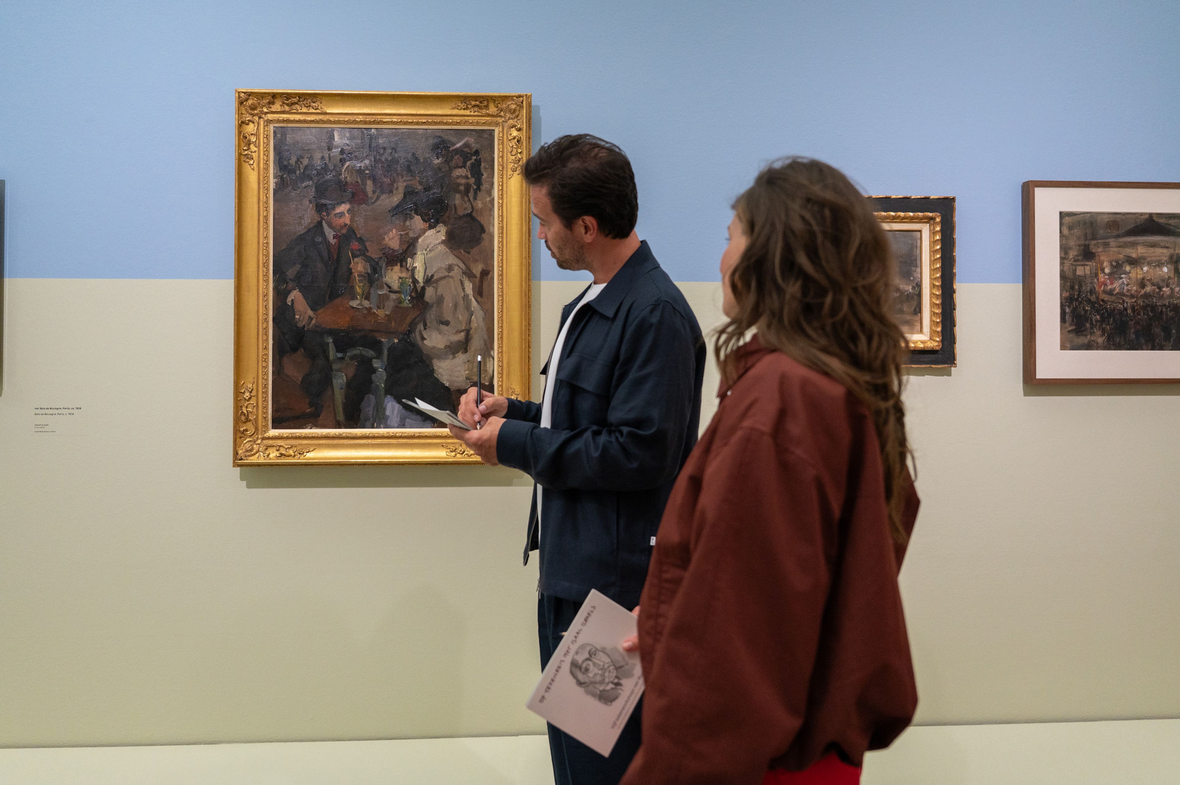 Twee bezoekers staan en tekenen bij een schilderij in een tentoonstelling