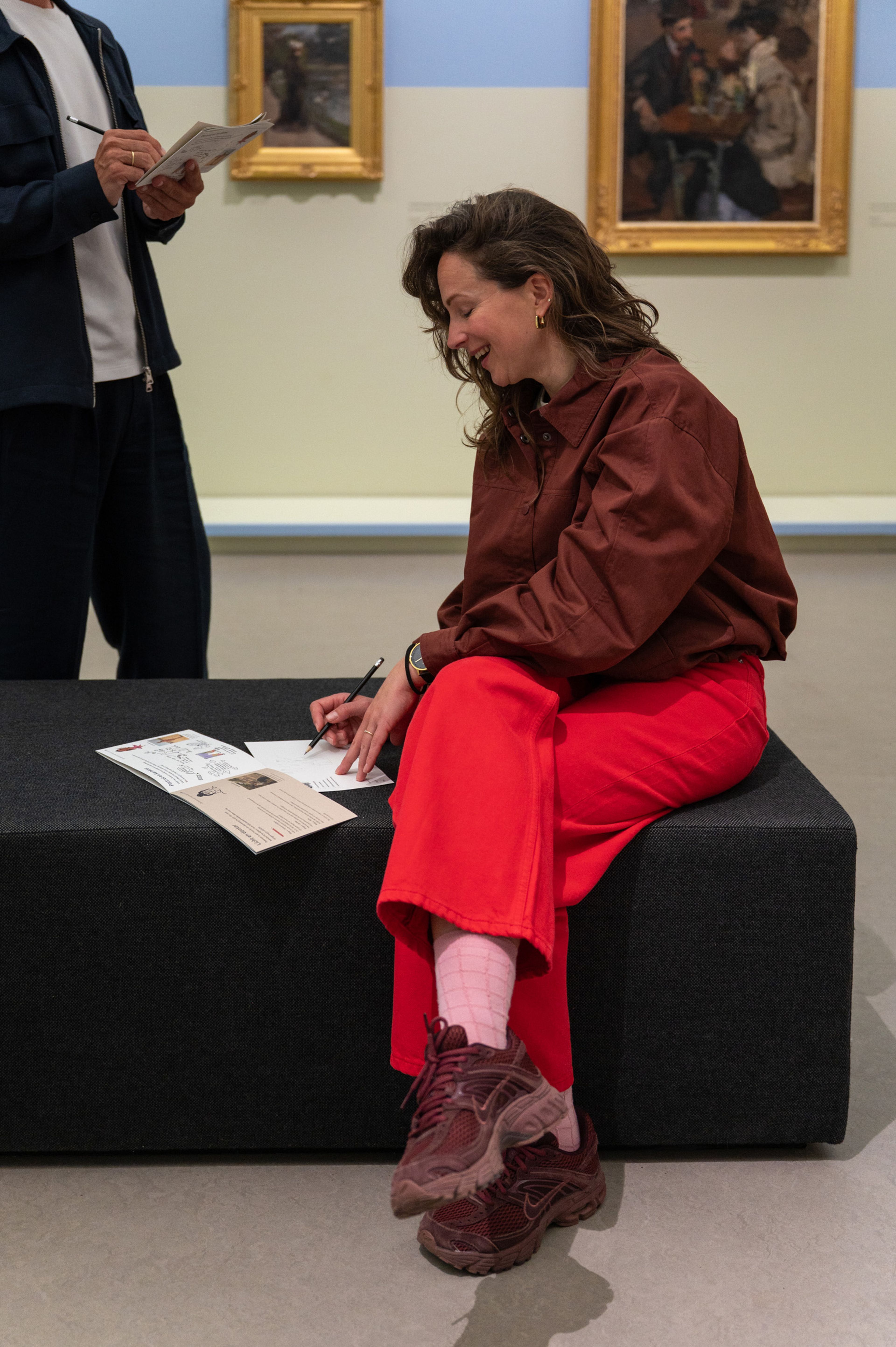 Bezoeker zit op een zwart bankje en tekent in een boek