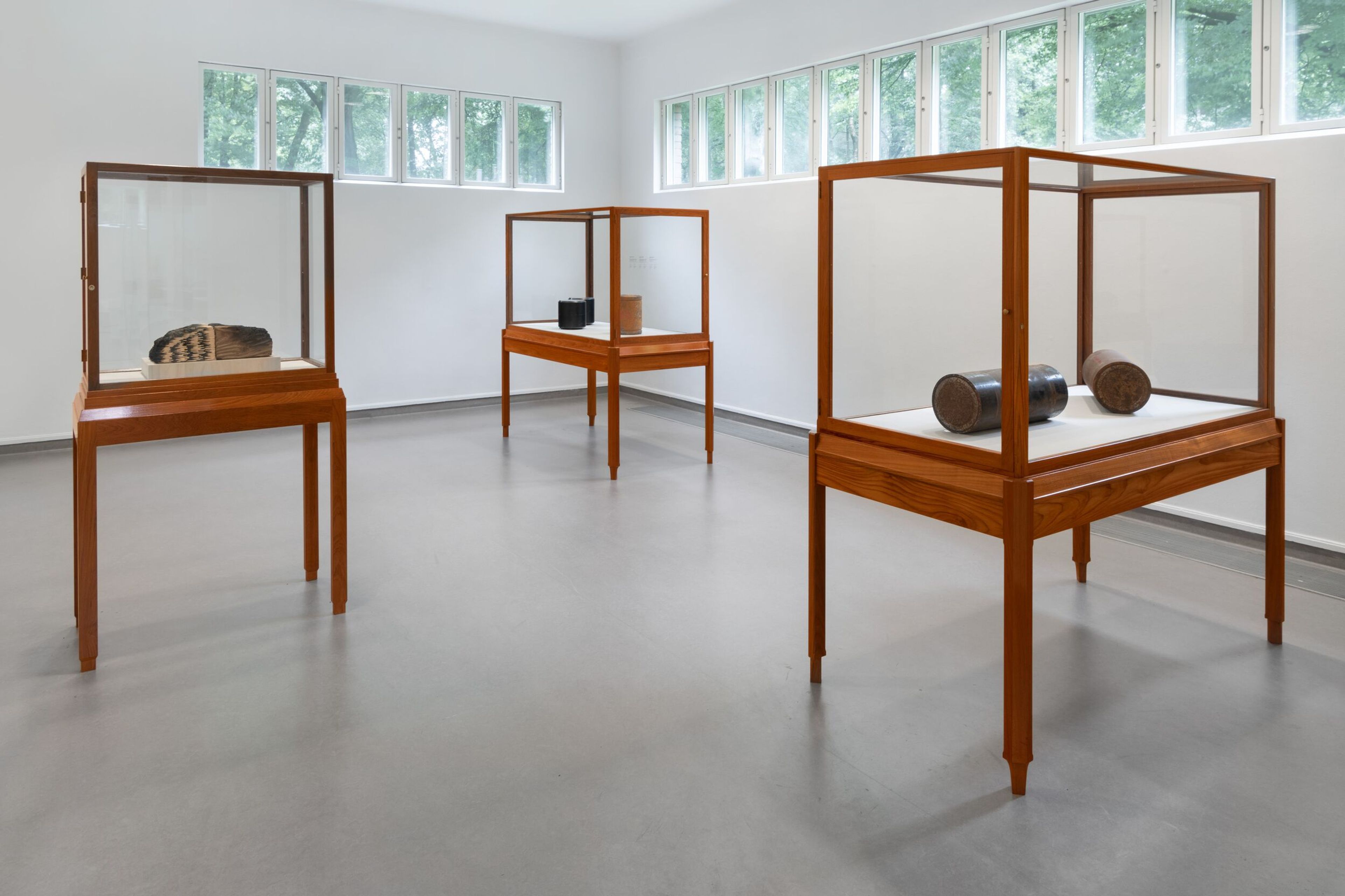 Photograph of a museum gallery containing three wooden display cabinets with glass panels, each containing works of art