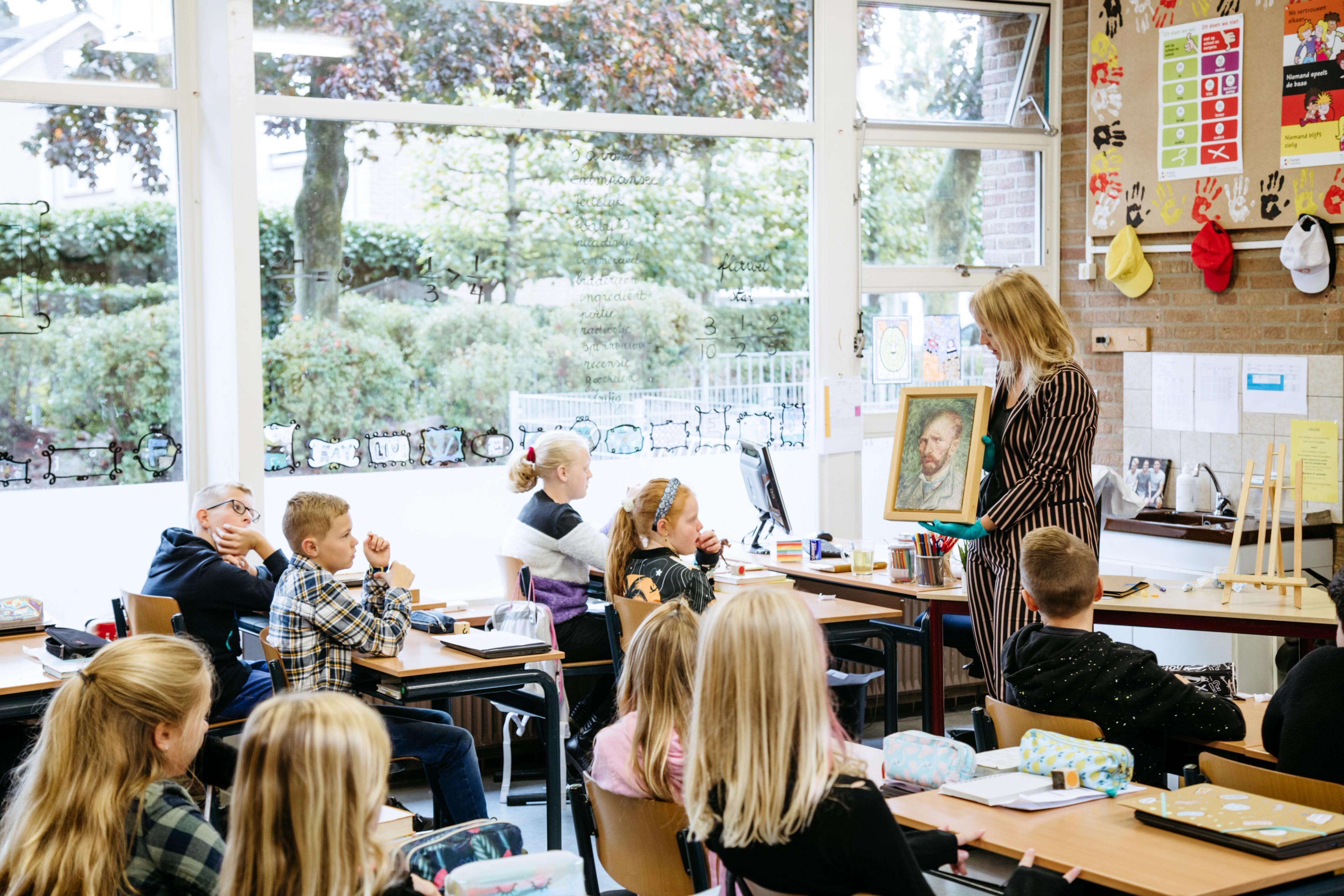 Museumdocent houdt een reproductie van 'Zelfportet' van Vincent van Gogh vast. Op de voorgrond kinderen in de klas