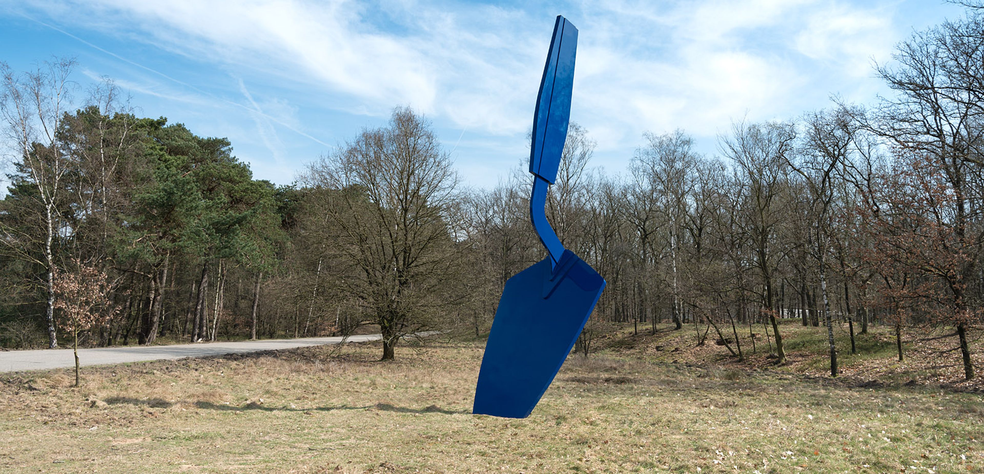 Grote blauwe buitensculptuur, geplaatst op grasveld met bomen op achtergrond. 