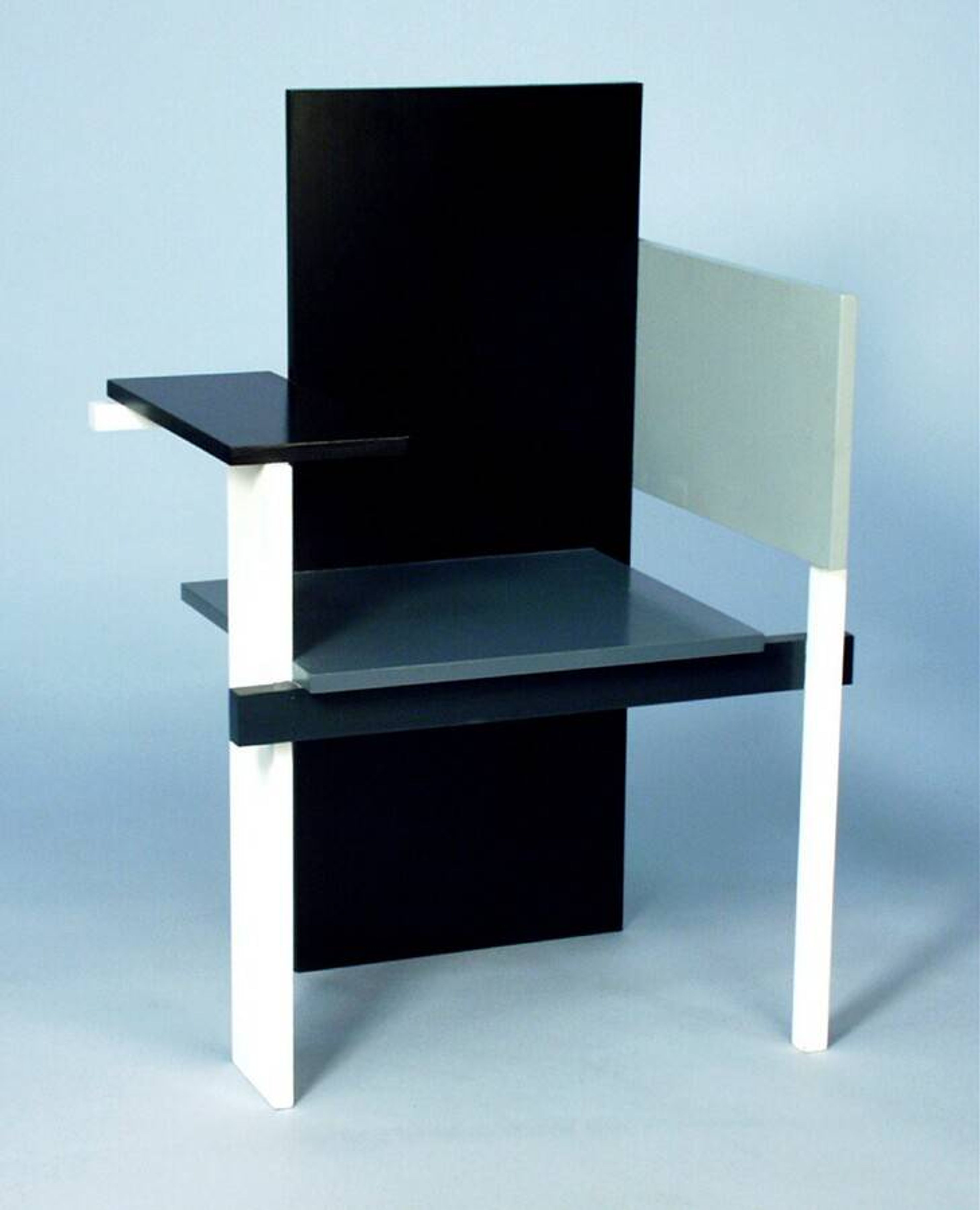 Foto van een moderne stoel met zwarte, witte en grijze vlakke panelen. Stoel heeft een asymmetrische rugleuning en armleuning, kenmerkend voor De Stijl, een kunst- en designbeweging. Gerrit Rietveld, Berlijnse stoel, ontwerp 1923, latere uitvoering