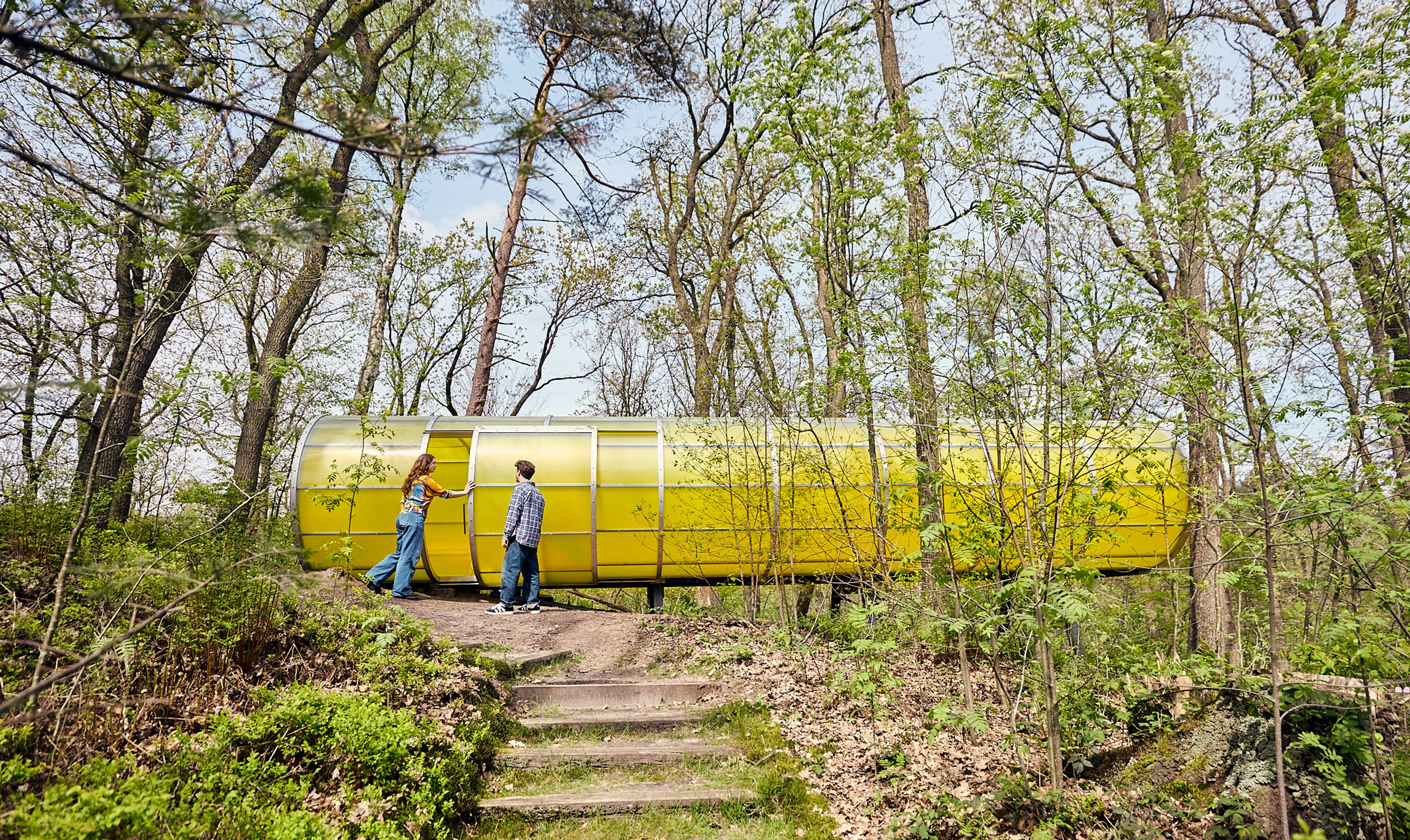Twee mensen bij een groot geel kunstwerk midden tussen de bomen in de beeldentuin