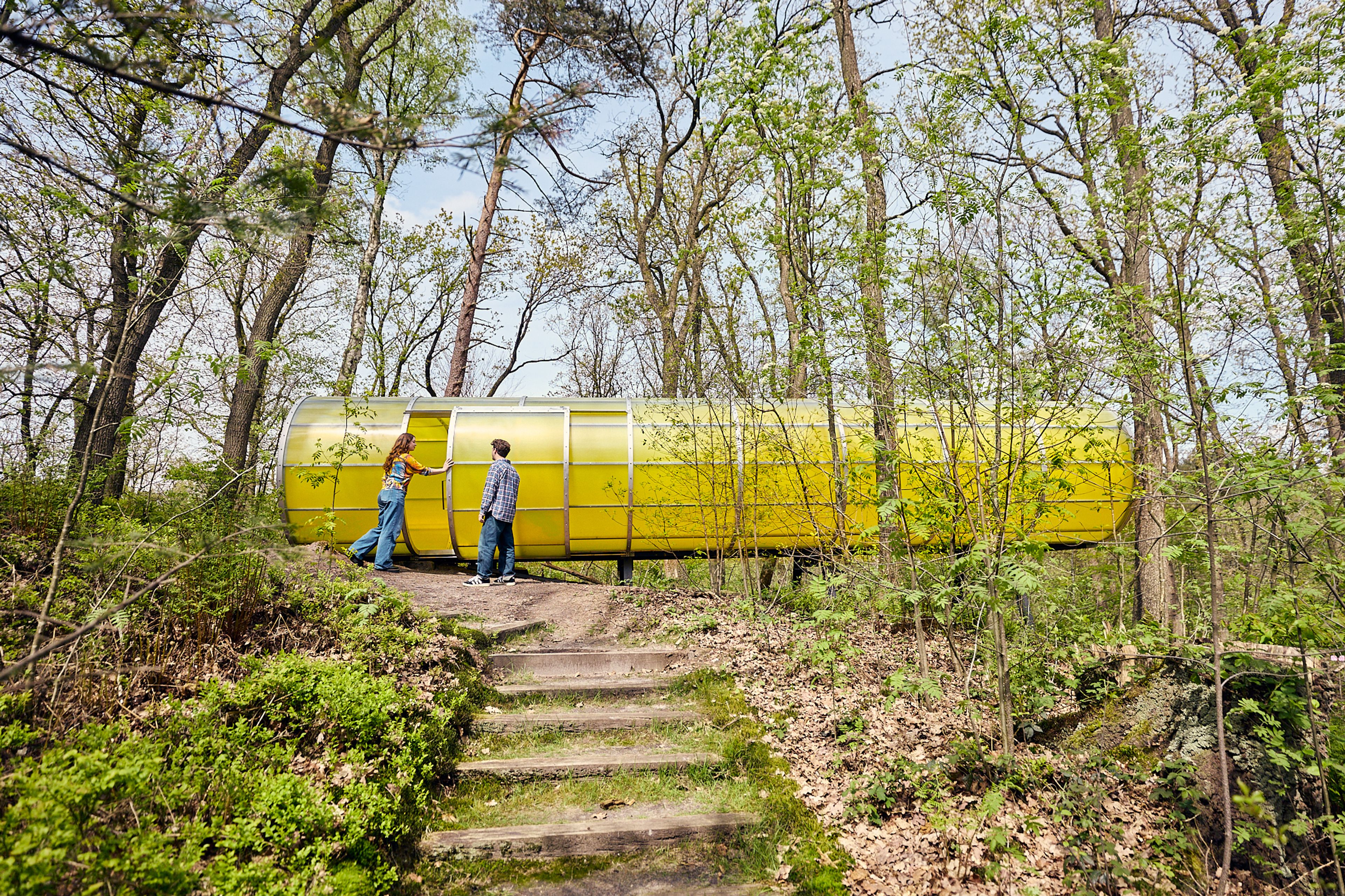 Twee mensen bij een groot geel kunstwerk midden tussen de bomen in de beeldentuin