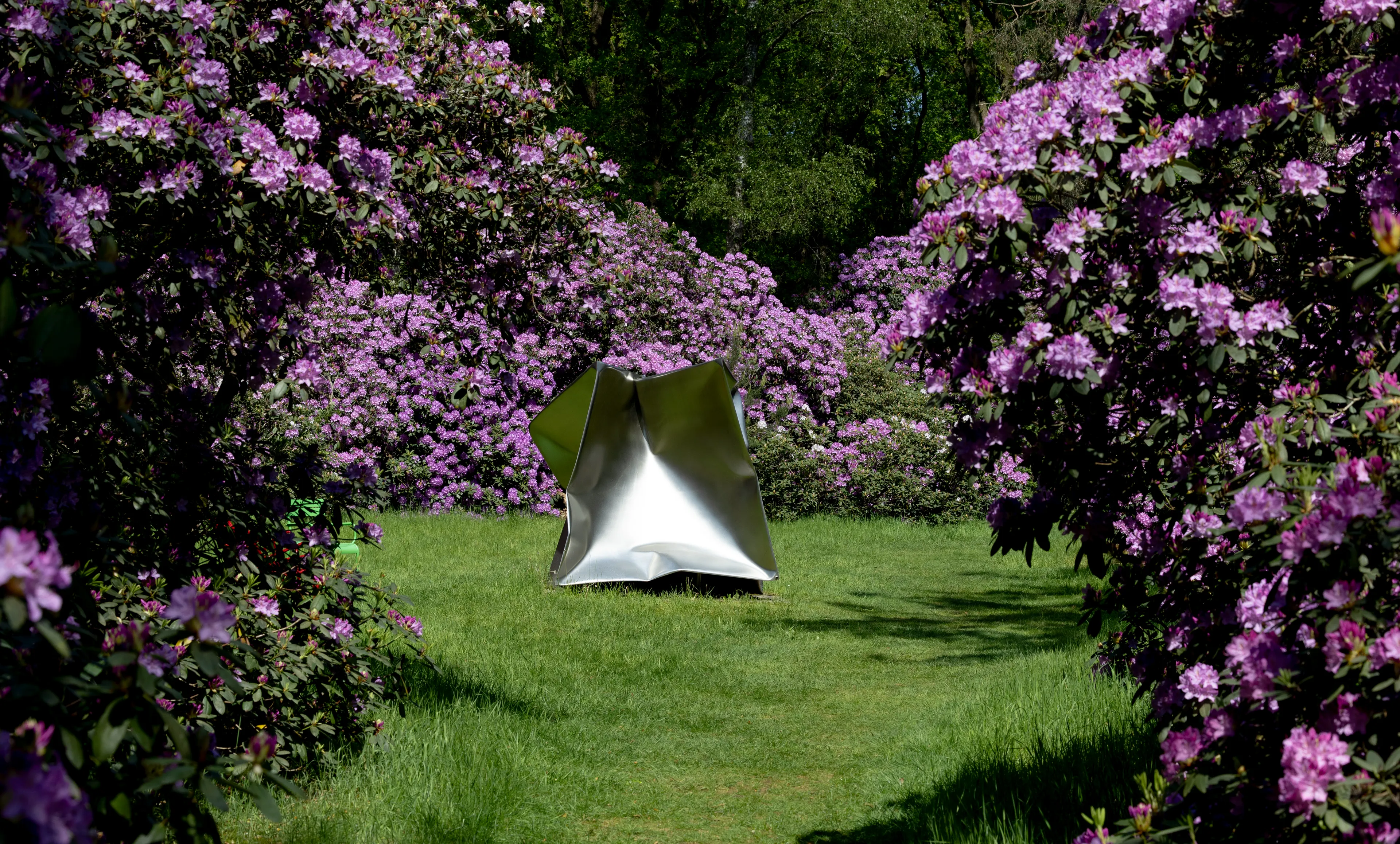 Zilveren vierkant kunstwerk midden in bloeiende rododendronstruiken