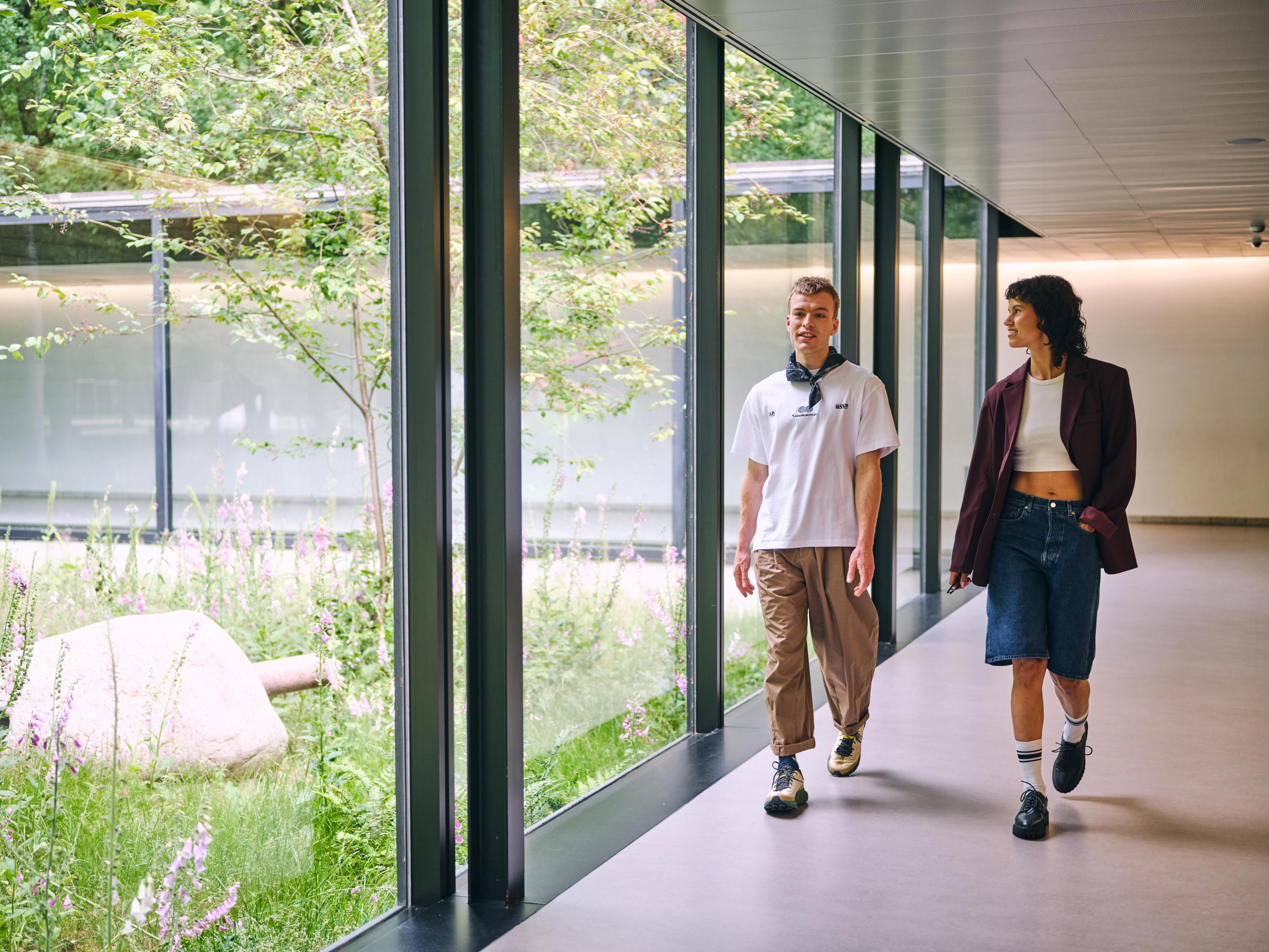 Twee personen wandelen door de gang met glazen ramen in het Kröller-Müller Museum